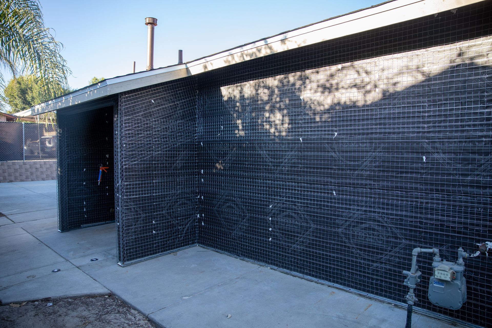 Black-tiled exterior wall with a covered walkway and concrete sidewalk in sunlight