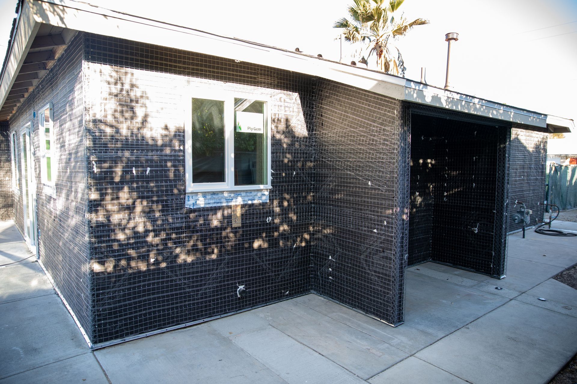 Black-tiled house exterior with a window and covered entryway along a concrete walkway