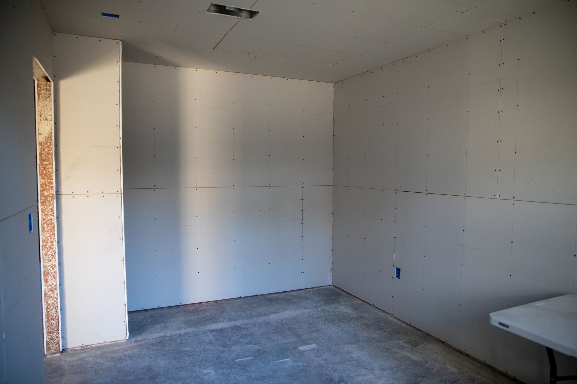 Empty unfinished room with white walls, bare concrete floor, and a doorway on the left.
