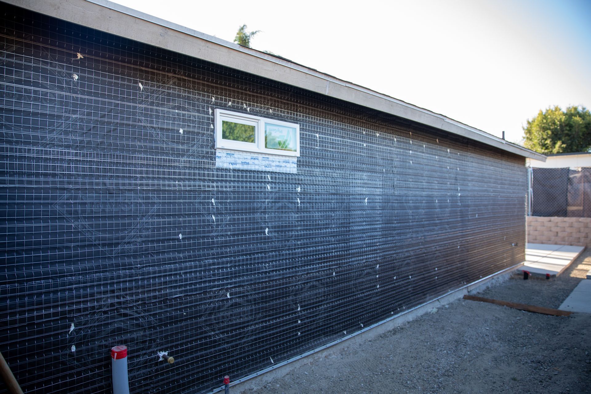 Dark tiled exterior wall with a small window and gravel path beside it