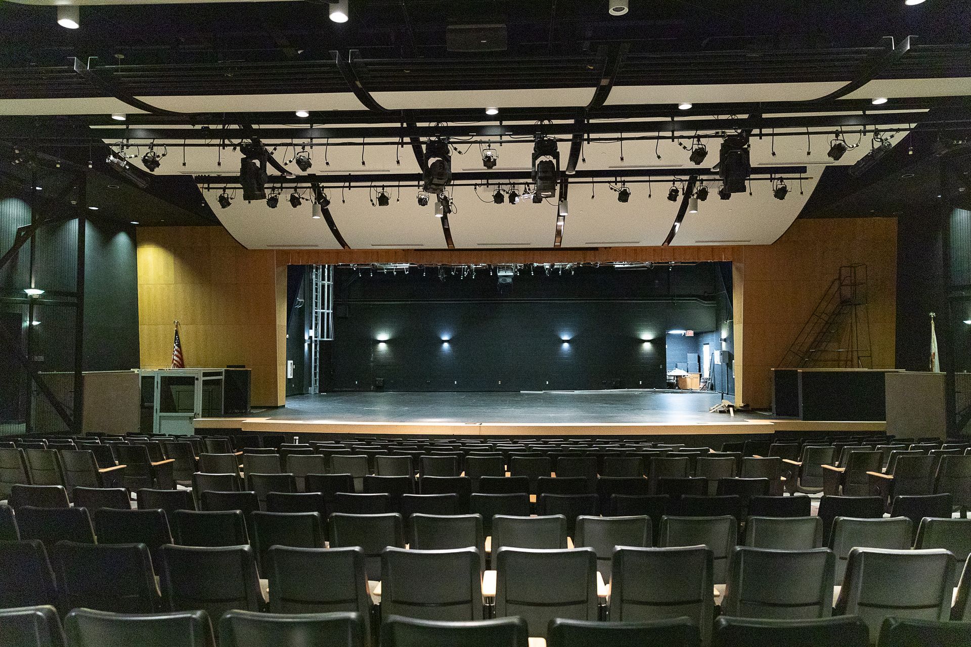 Empty theater auditorium with rows of seats facing a lit stage and black backdrop.
