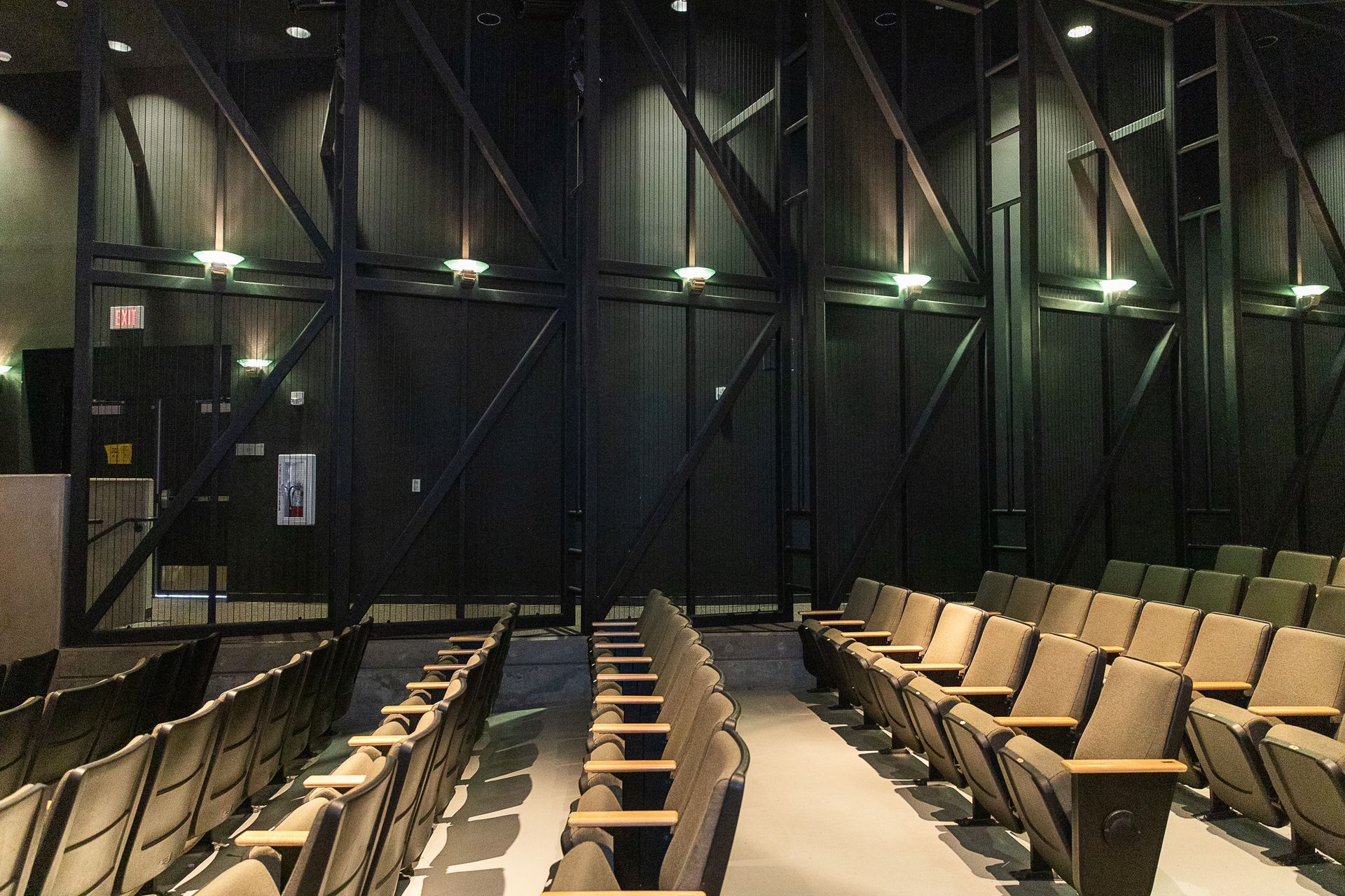 Empty auditorium with rows of tan seats, dark walls, and ceiling lights in a theater setting