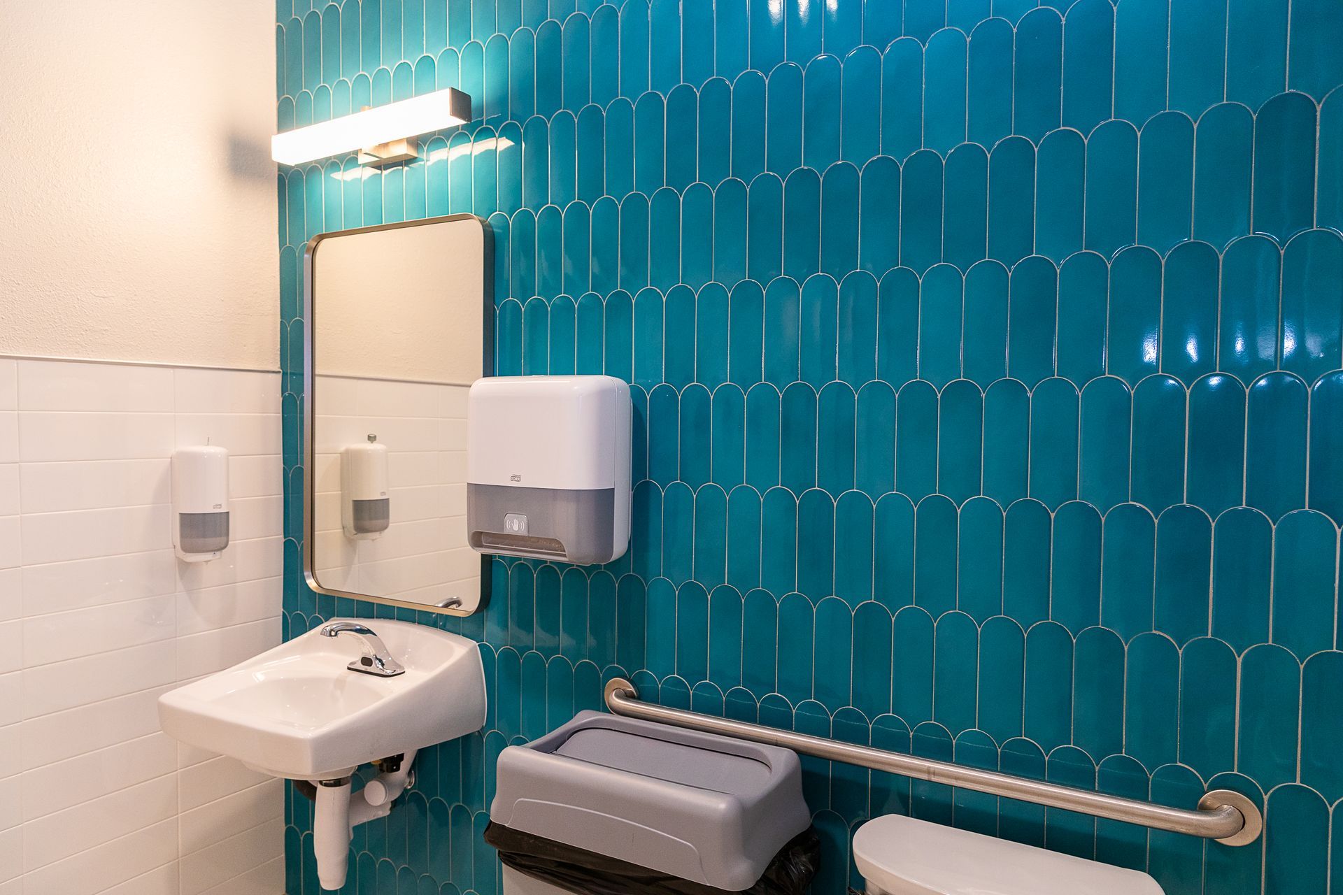 A bathroom with blue tiles , a sink , a toilet and a mirror.