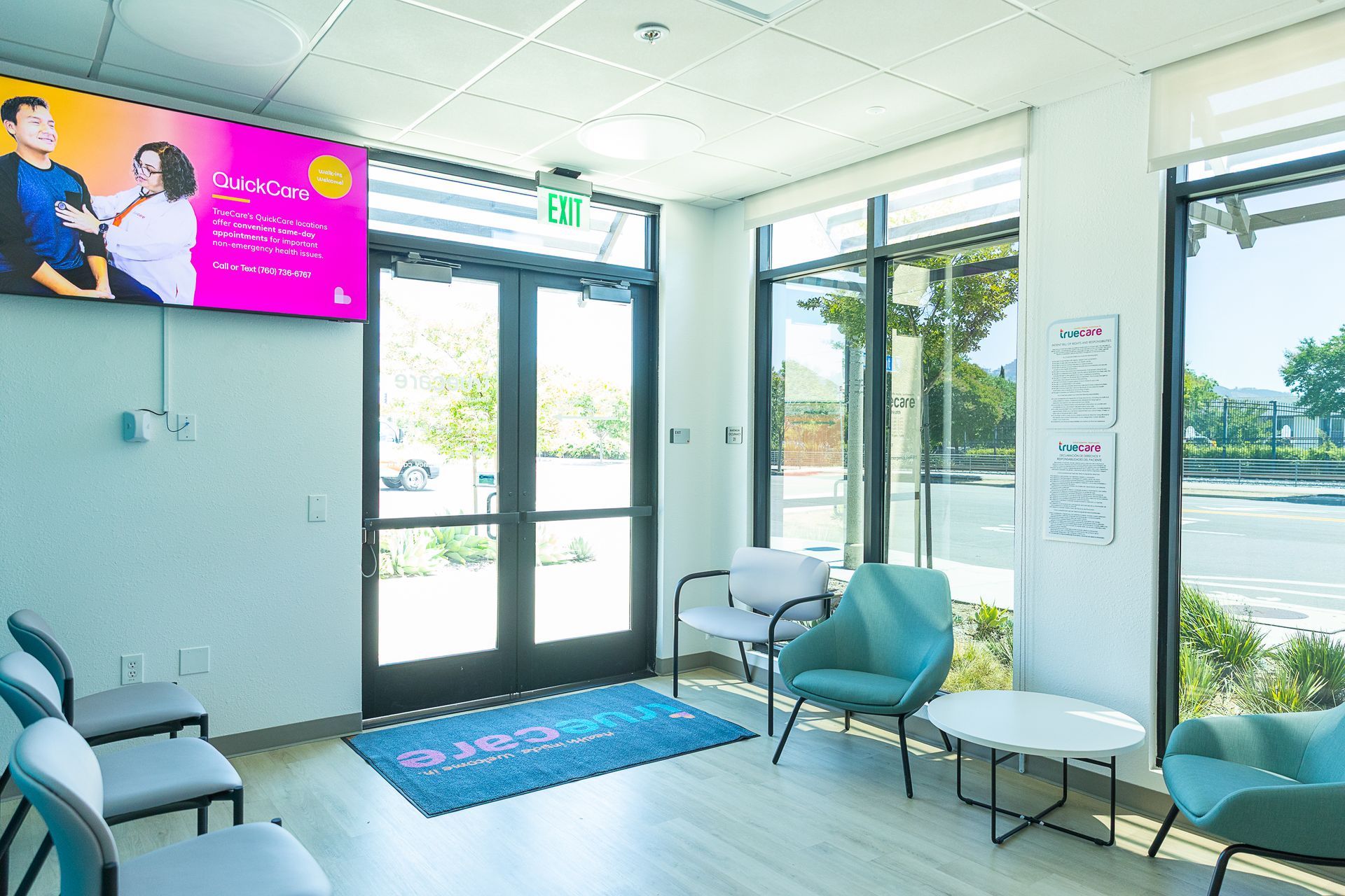 A waiting room with chairs , tables and a large screen on the wall.