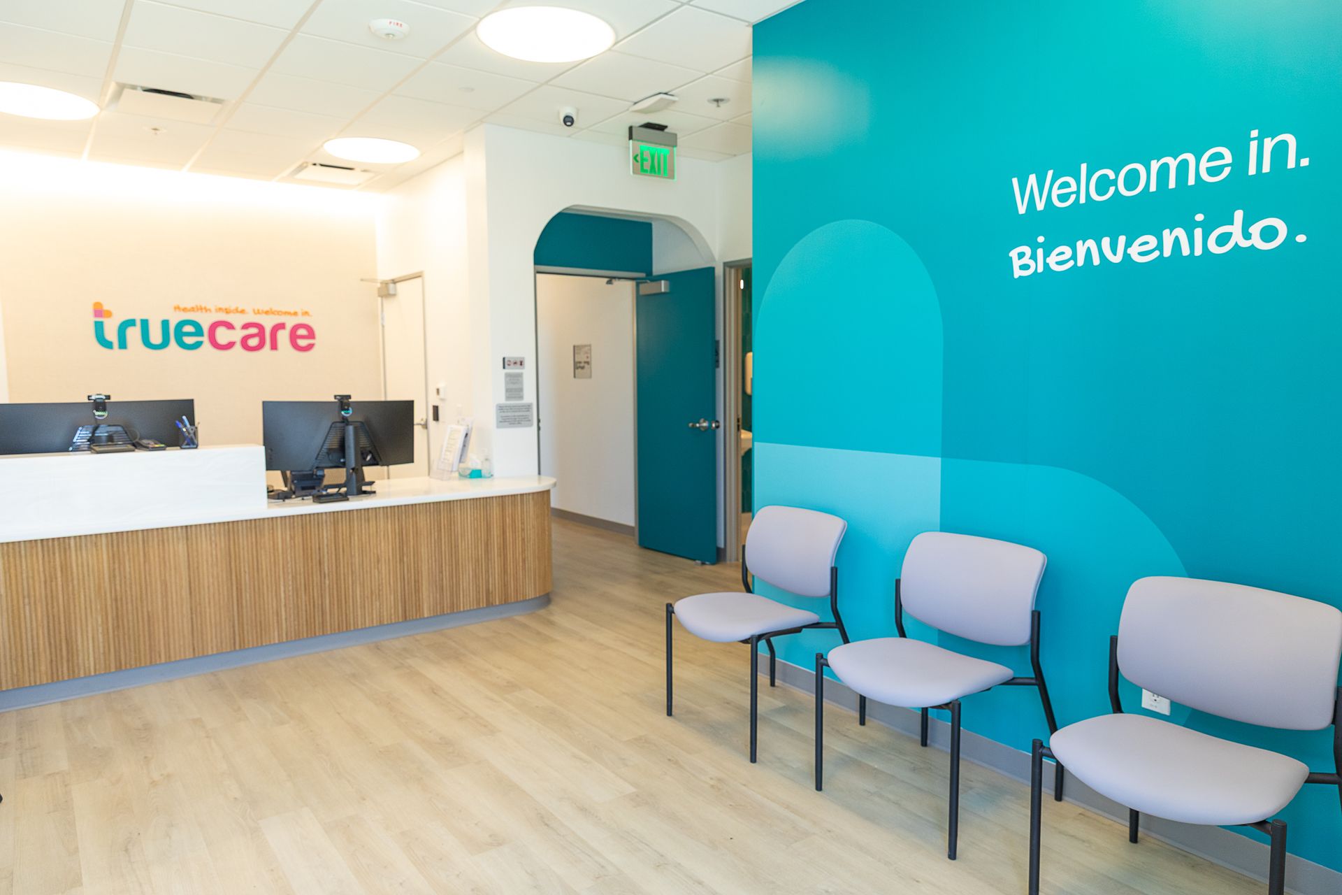 Bright clinic reception with wood desk, blue accent wall, and chairs beneath “Welcome in” sign