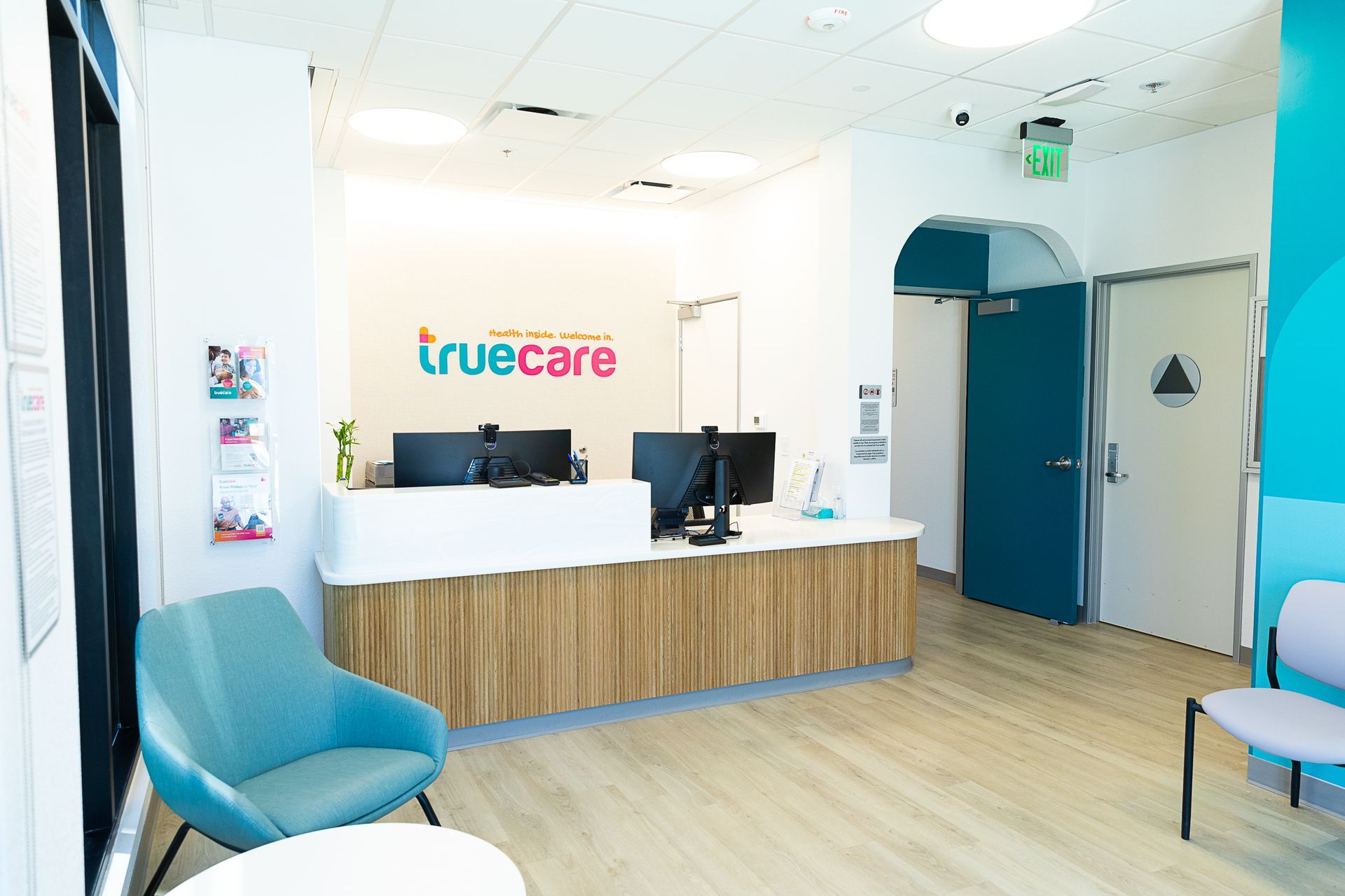 A waiting room with a desk and chairs and a truecare logo on the wall.