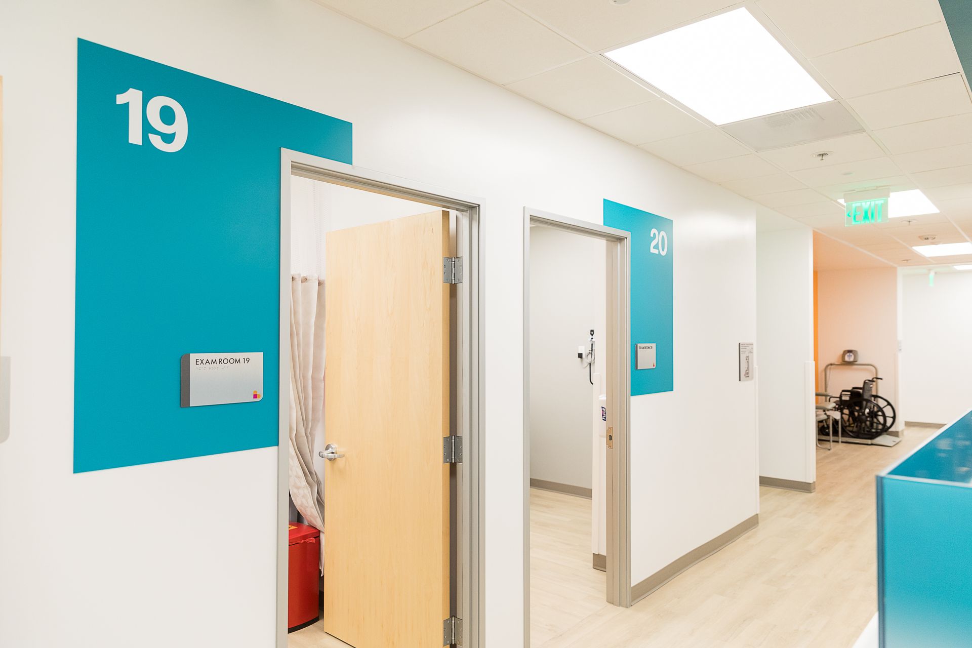 A hallway in a hospital with a wheelchair in the corner.