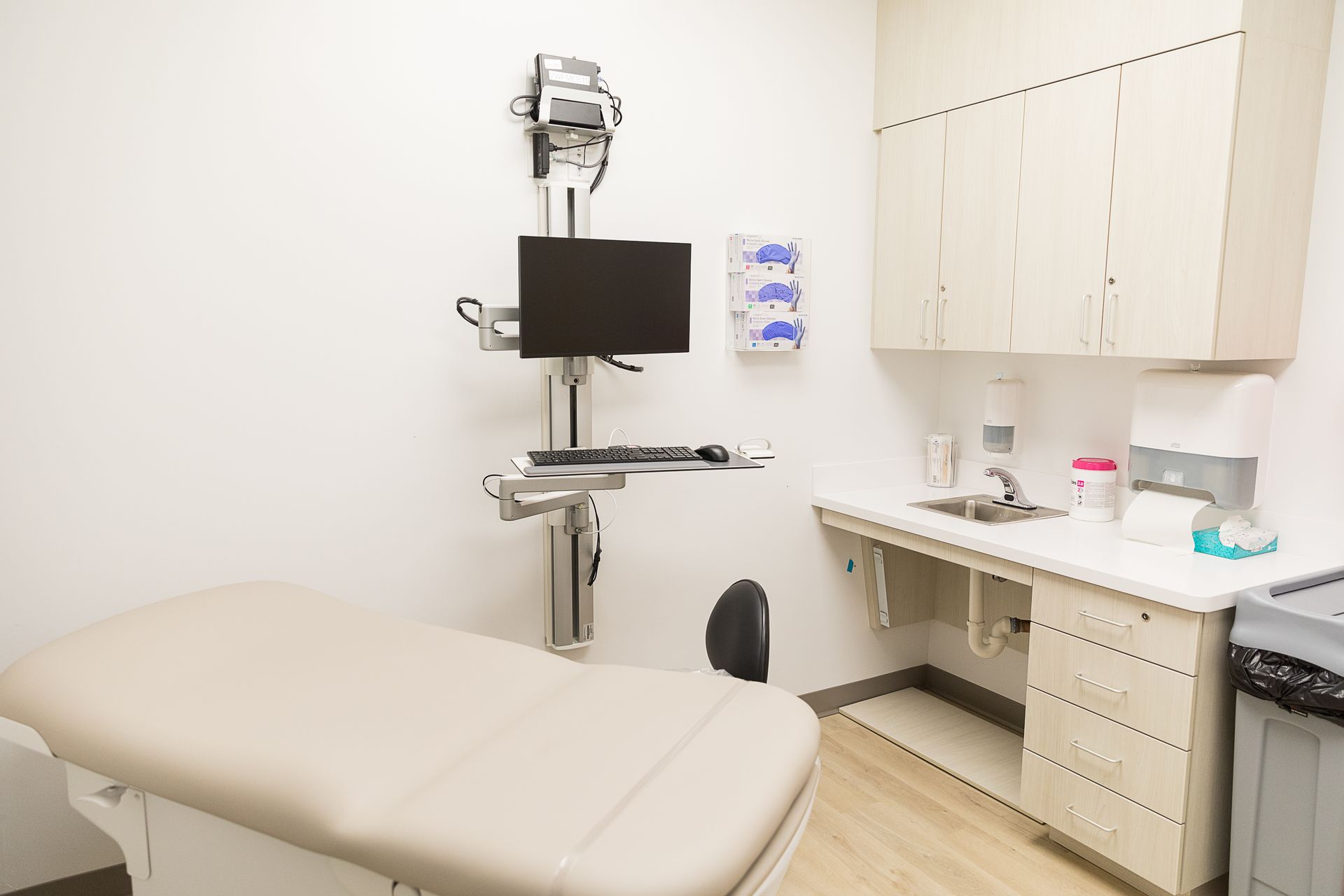 A doctor 's office with a bed , desk , computer and monitor.