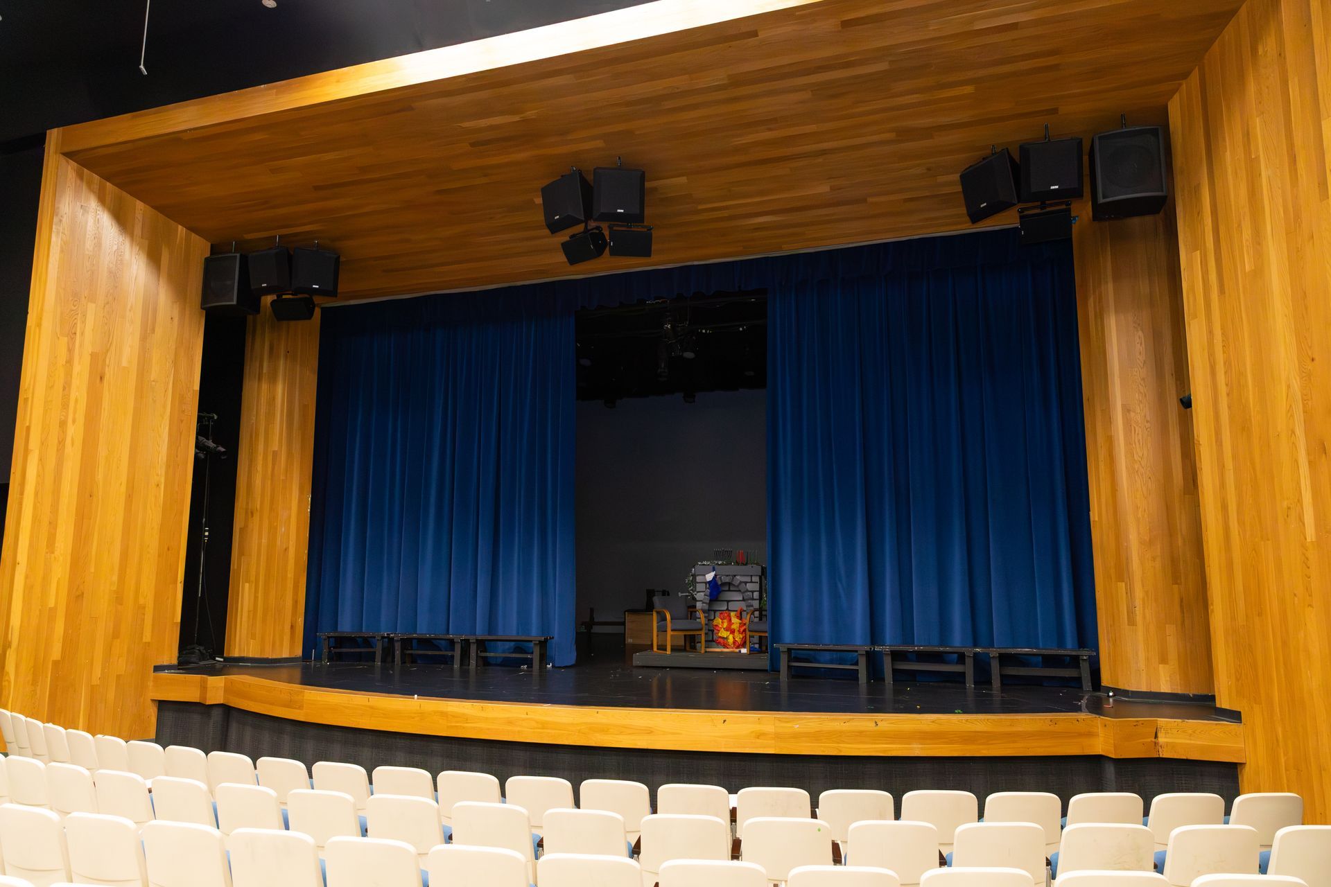 Empty auditorium stage with blue curtains, wooden walls, and rows of seats in front