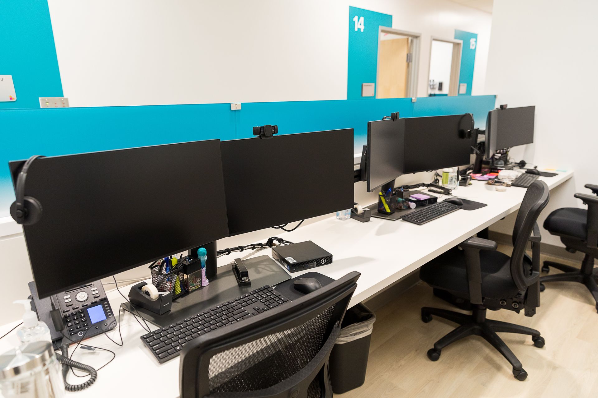 A row of desks with computers and chairs in an office.