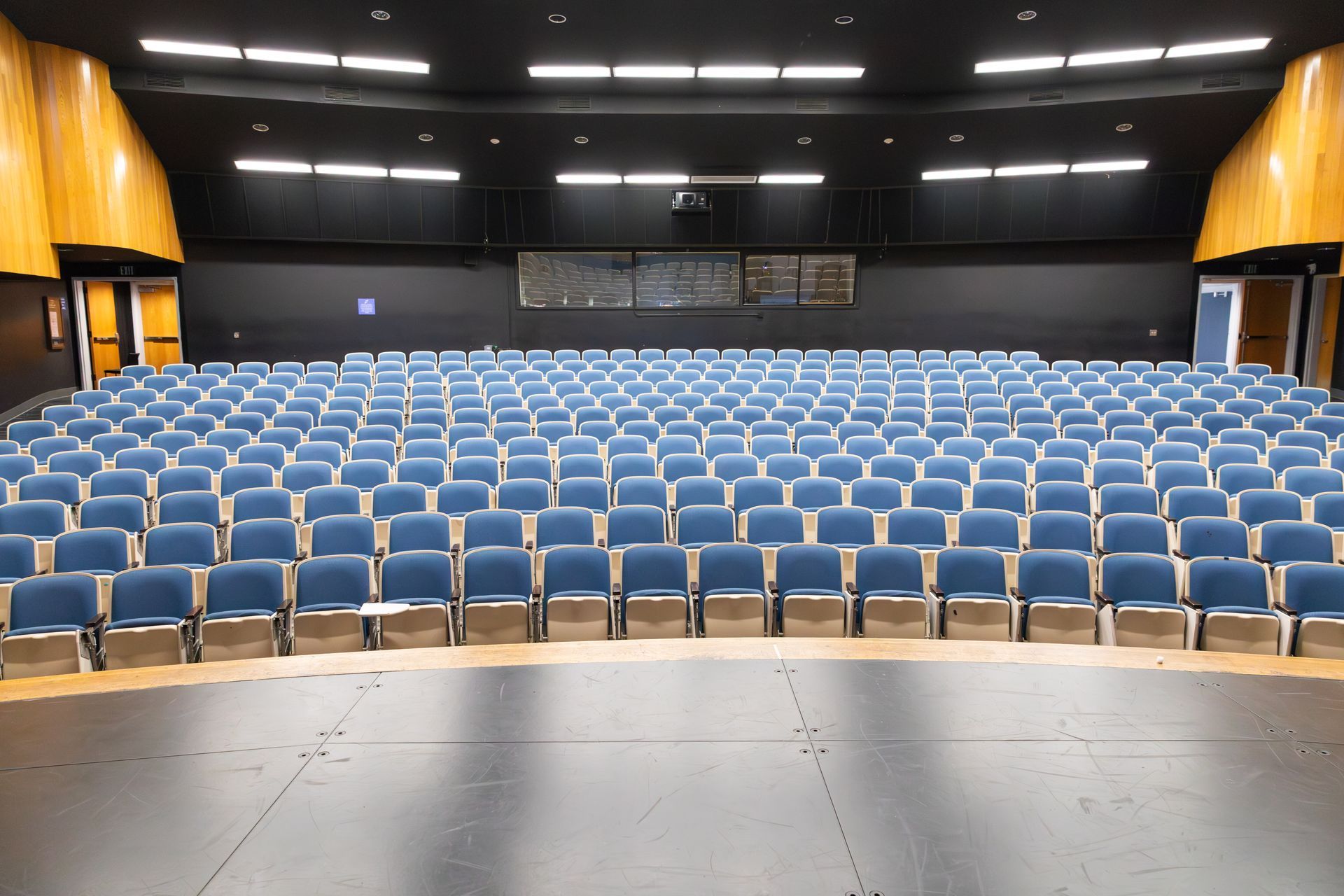 Empty auditorium with rows of blue seats and a stage under bright overhead lights