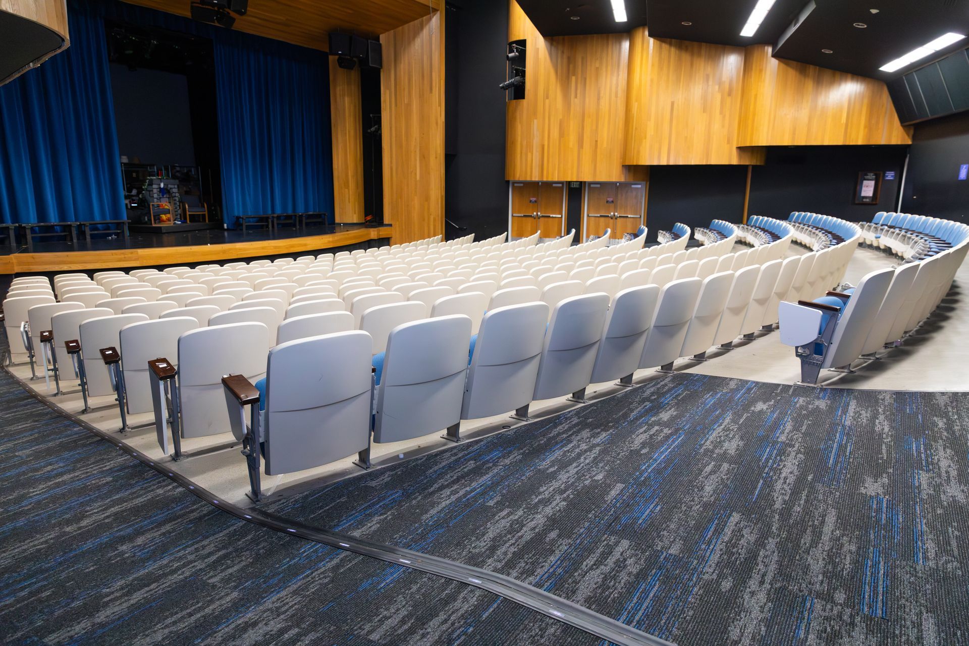 Empty auditorium with rows of white seats, blue curtains, and wood-paneled walls