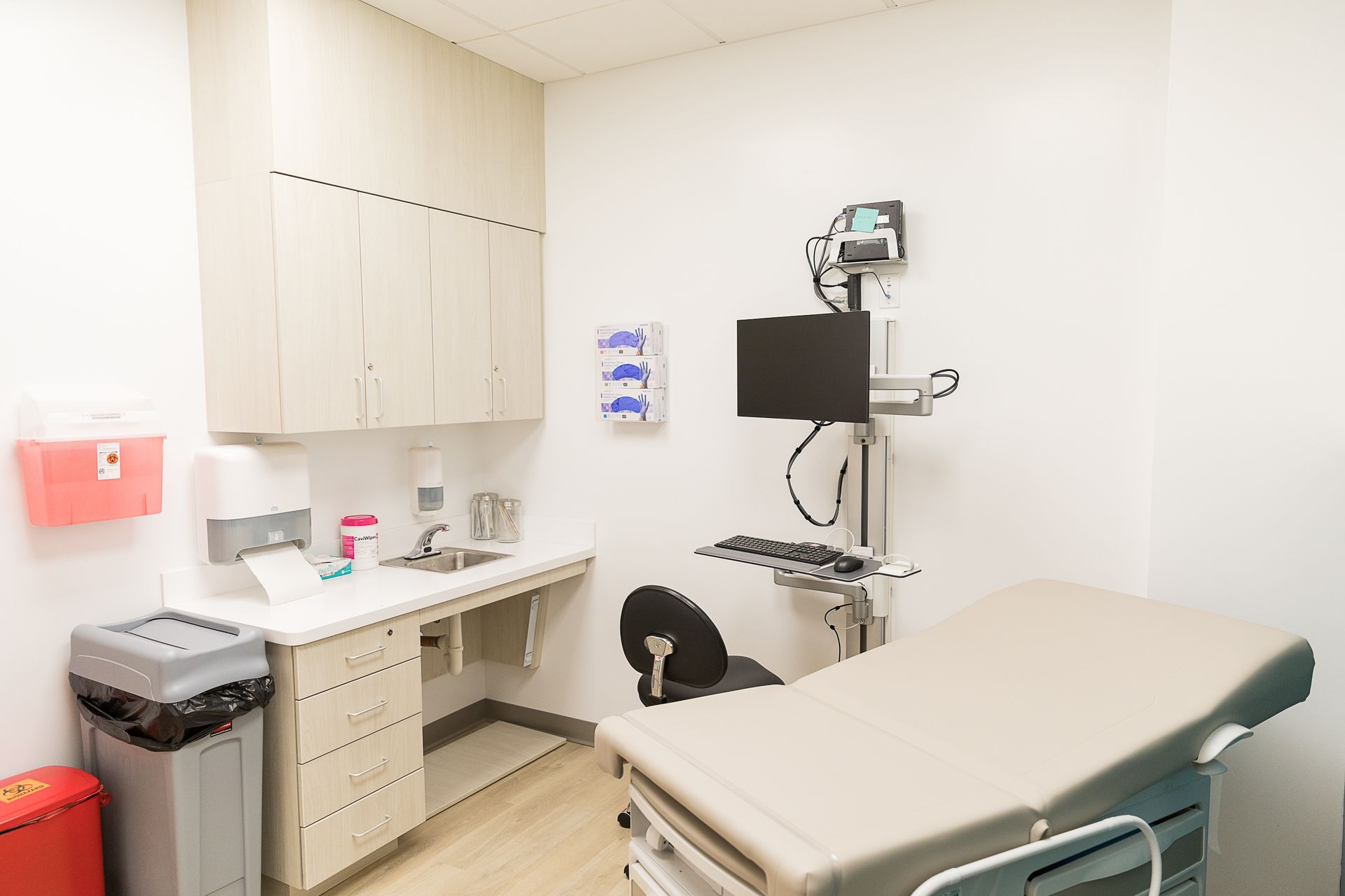 A doctor 's office with a desk , chair , sink and computer.