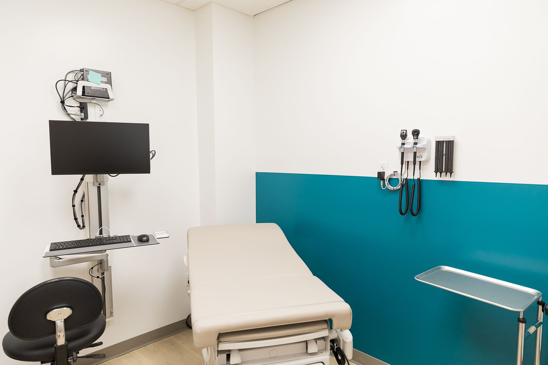 A doctor 's office with a bed , chair , computer and monitor.