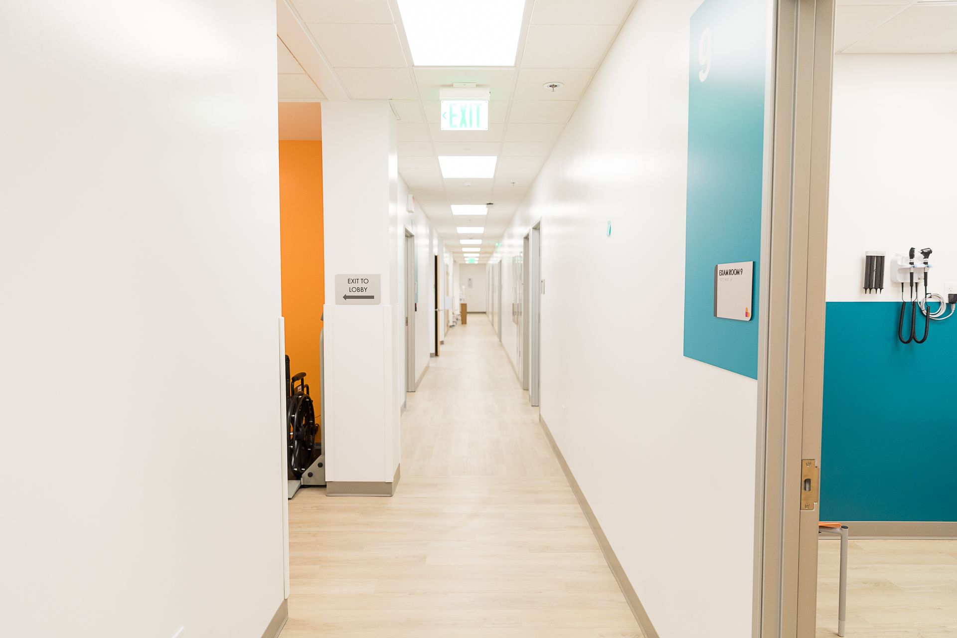 A long hallway in a hospital with white walls and wooden floors.