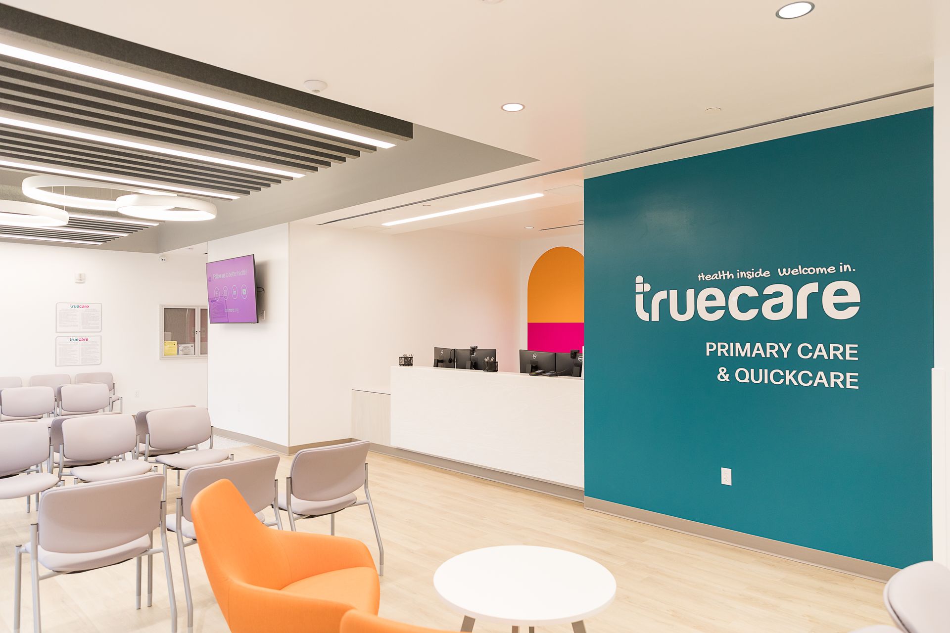 A waiting room with chairs , a table and a sign that says truecare primary care and quickcare.