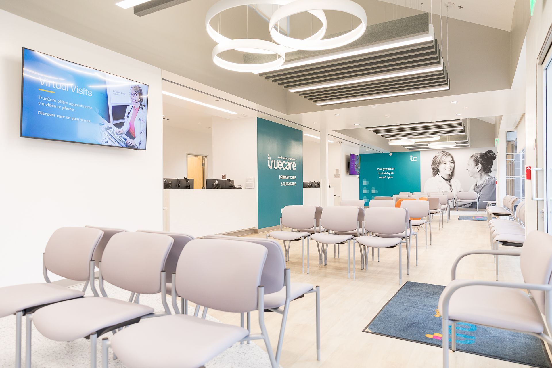 A waiting room with lots of chairs and a tv on the wall.