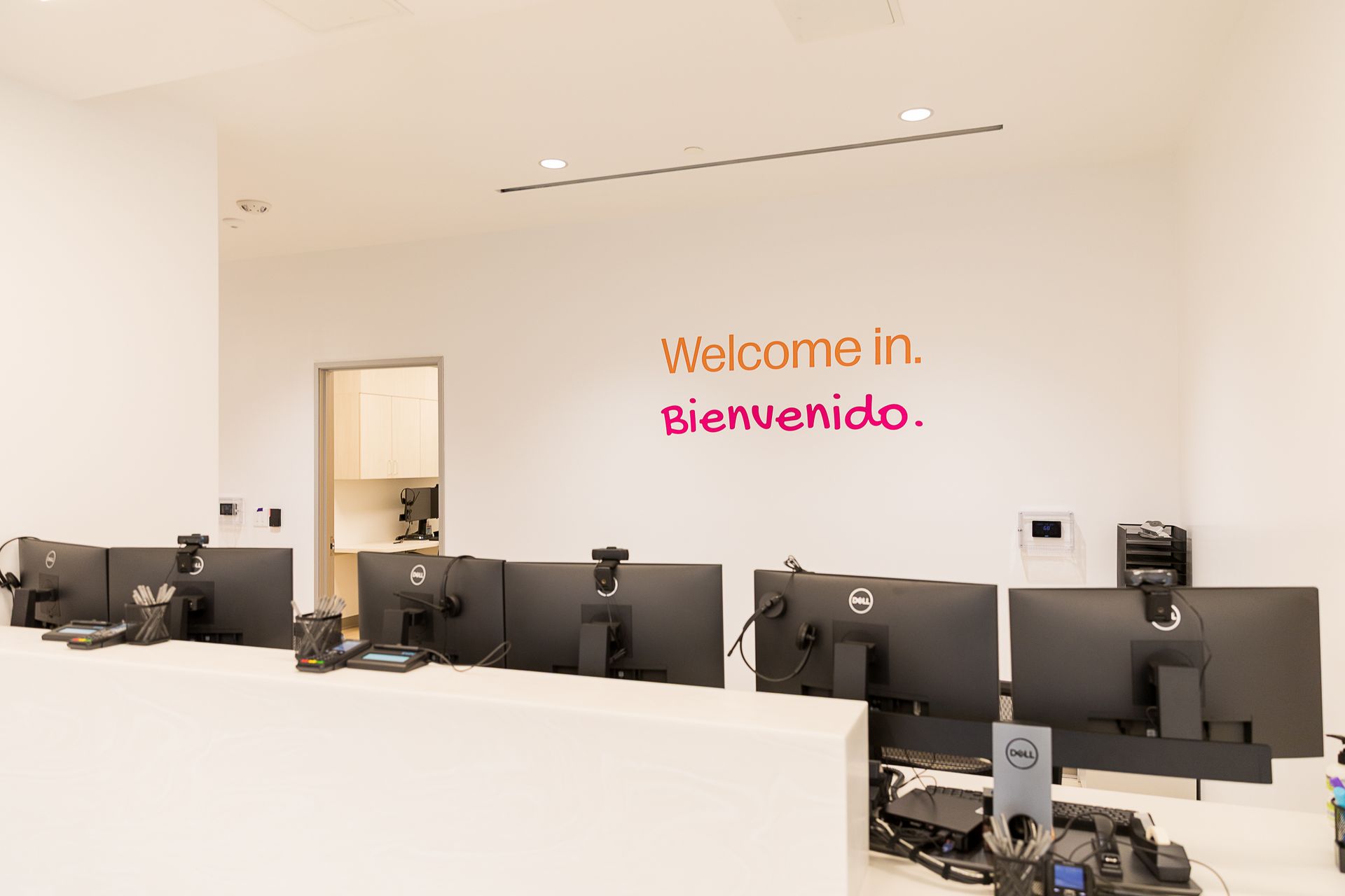 A row of computer monitors in an office with a sign on the wall that says `` welcome in , bienvenido ''.
