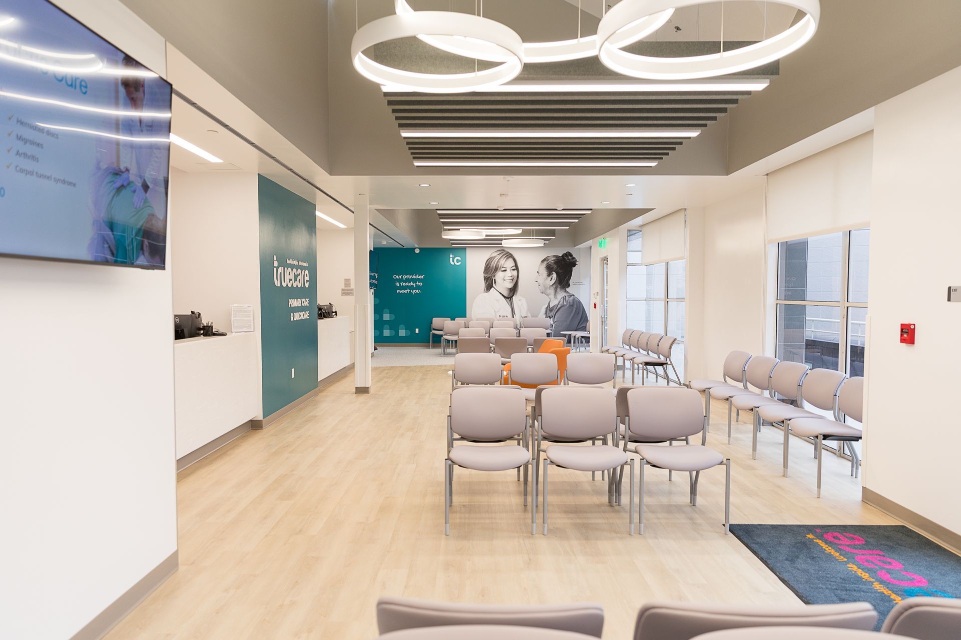 A waiting room with a lot of chairs and a tv on the wall.