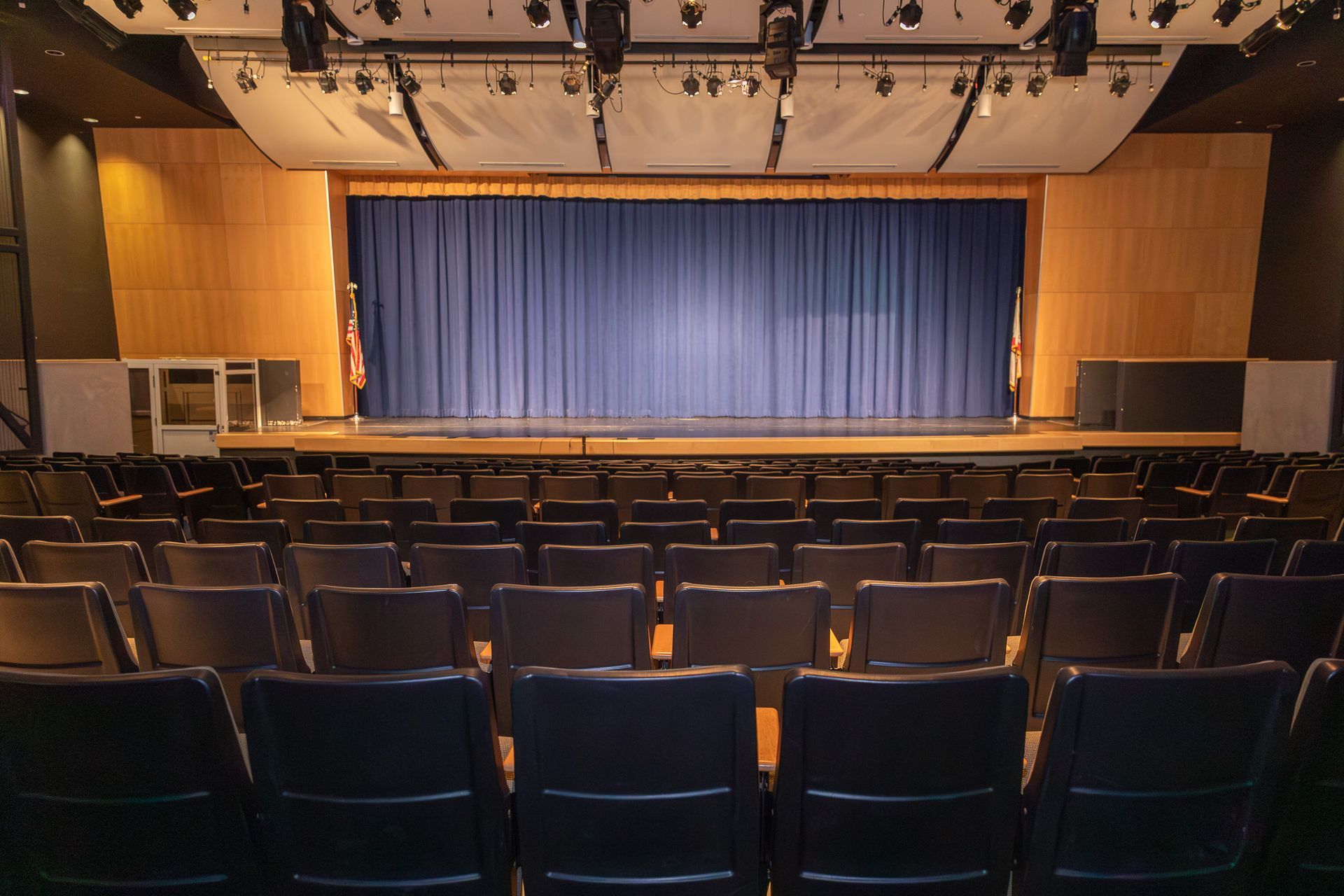 Empty theater auditorium with rows of seats facing a stage with closed blue curtains
