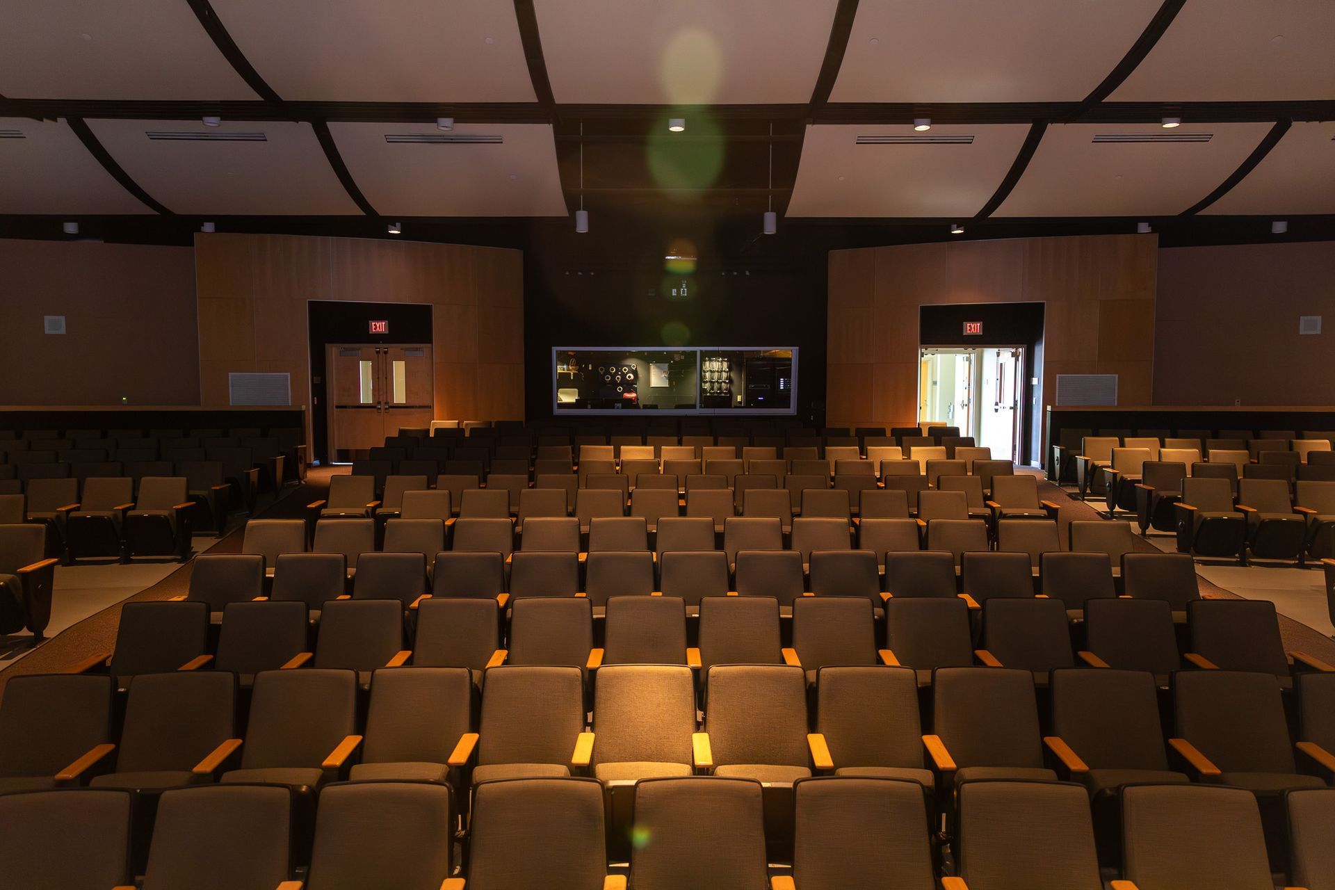 Empty auditorium with rows of brown seats and a stage at the front, viewed from the back.