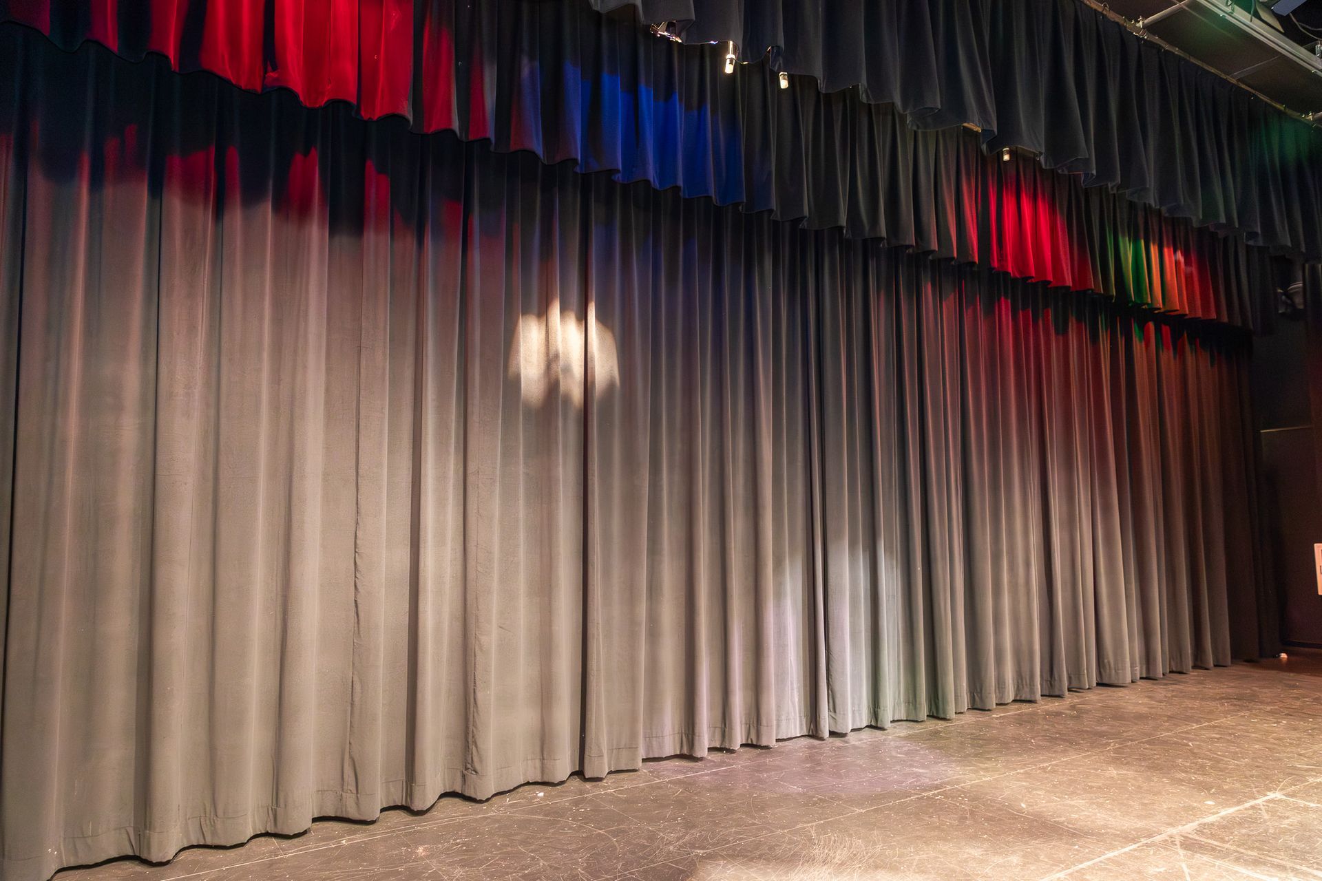 Closed gray stage curtain with red and blue lights above it