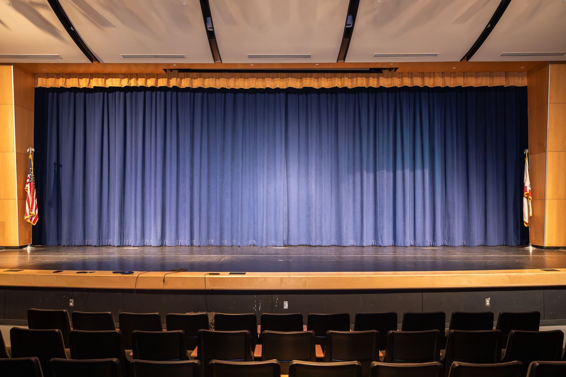 Empty theater stage with blue curtain and rows of seats in front