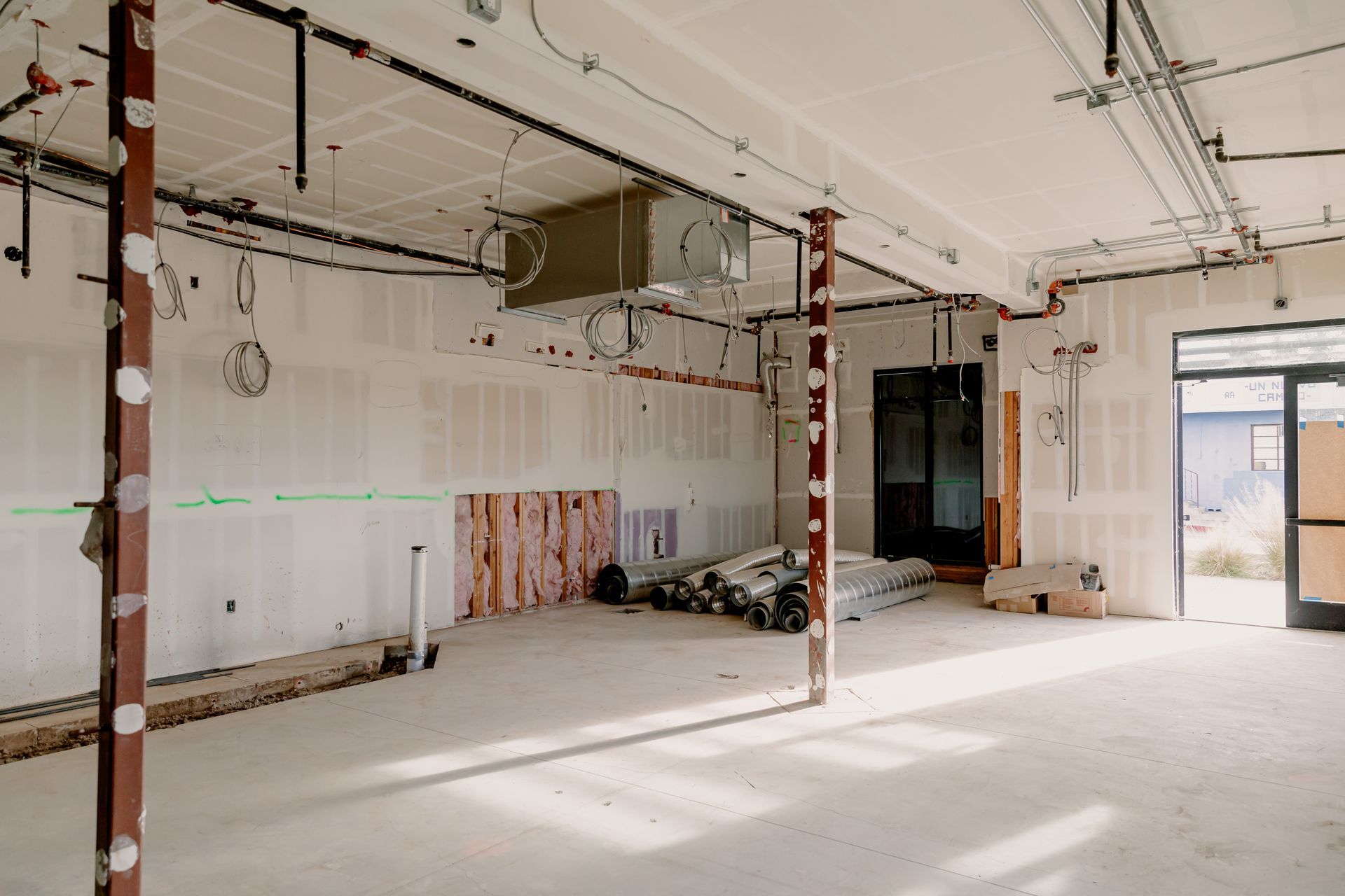 Empty room under renovation with exposed ceiling, bare walls, and sunlight through a window.