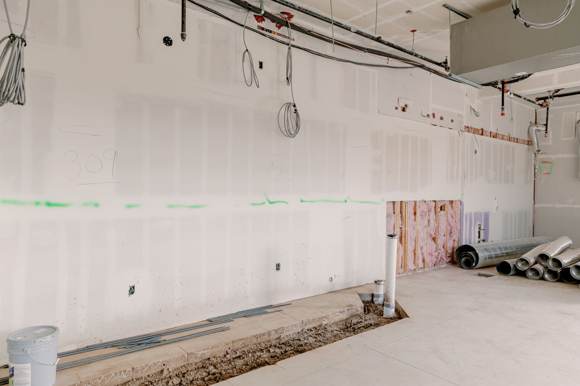 Unfinished room with white drywall, exposed ceiling pipes, and construction materials on the floor.