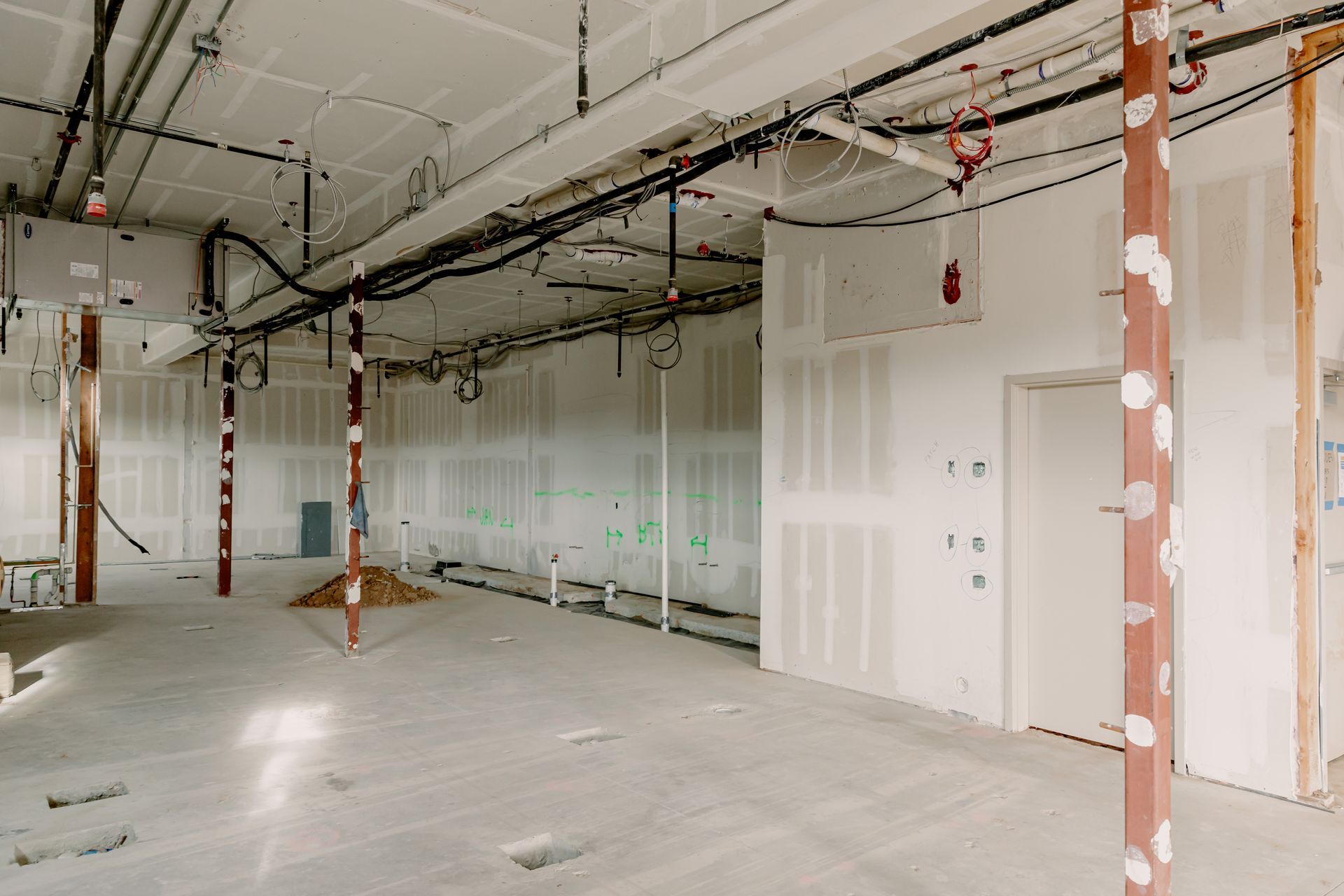 Empty unfinished interior with exposed ceiling pipes, white walls, and construction columns