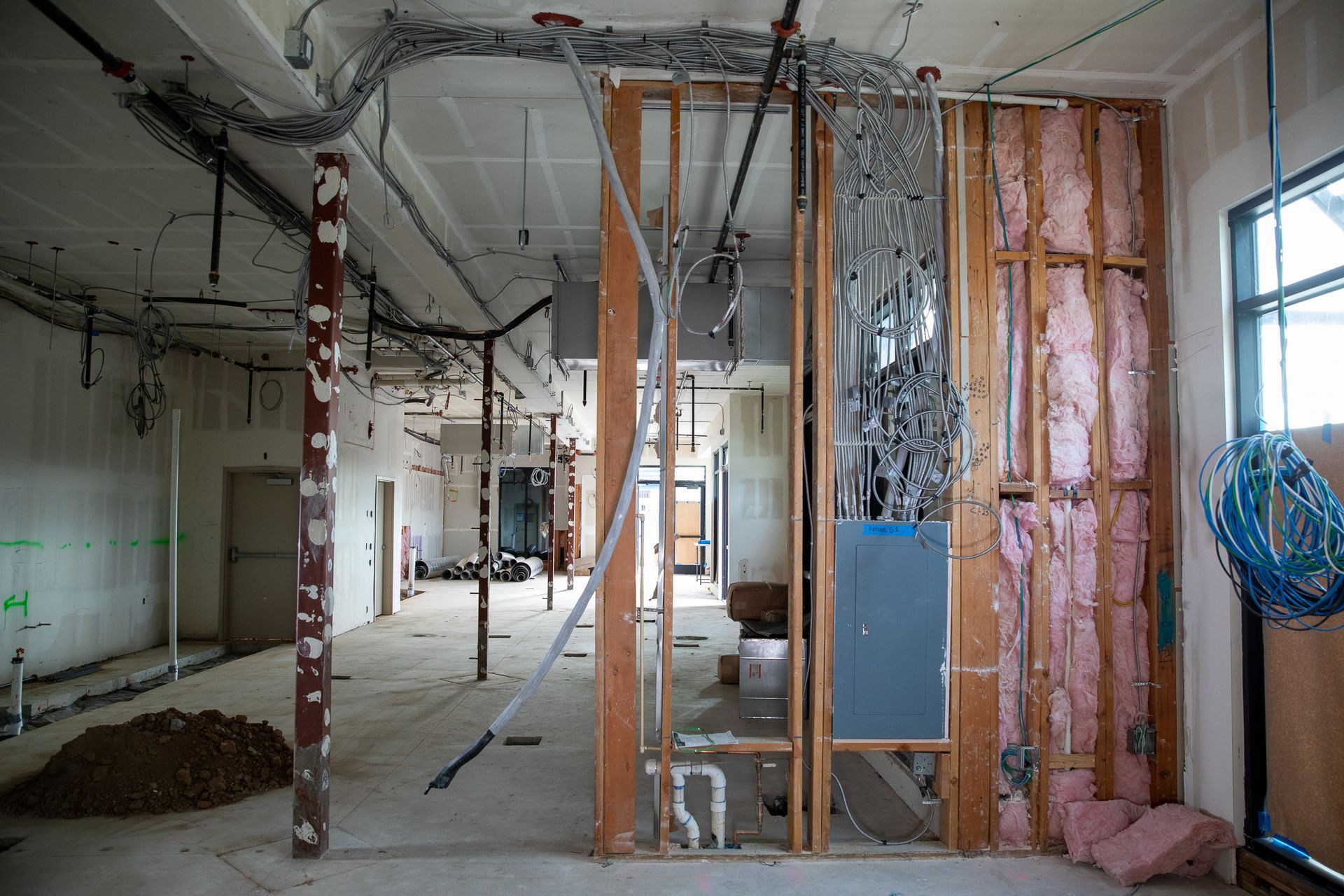 Interior of a house under renovation, with exposed framing, hanging wires, and insulation panels.