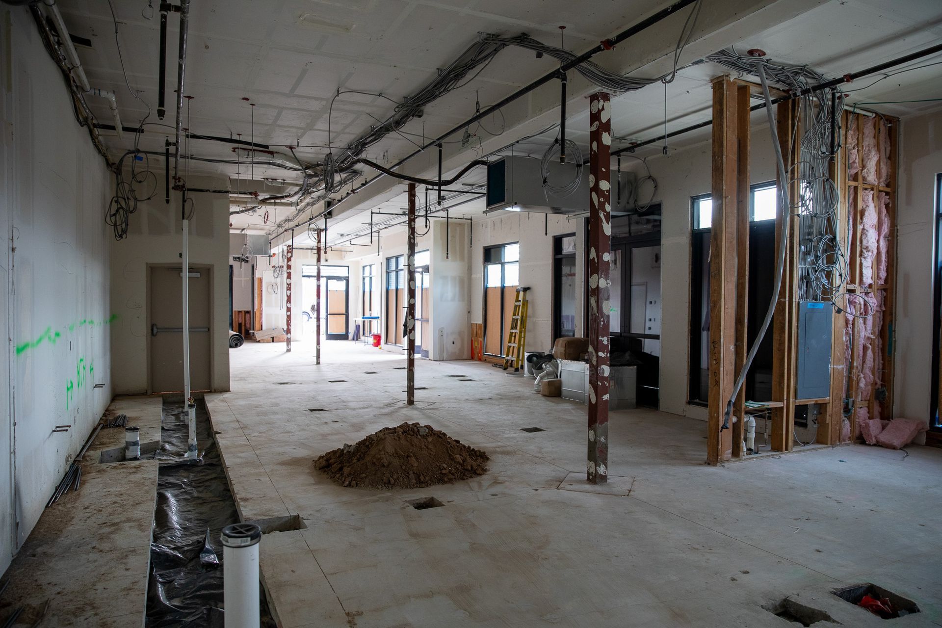 Abandoned, unfinished office interior with exposed walls, hanging wires, and construction debris on the floor
