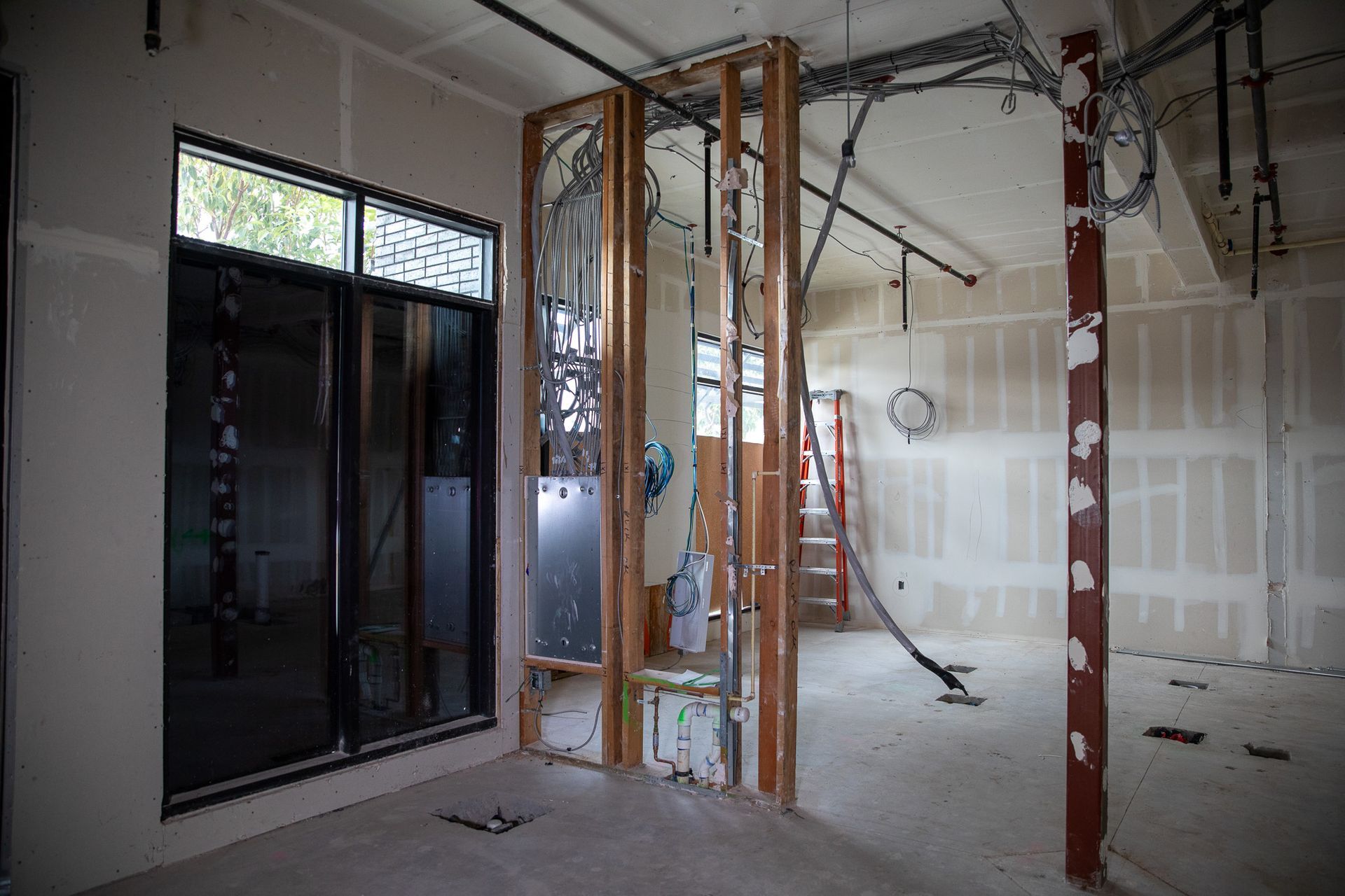 Partially renovated room with exposed framing, hanging wires, and sliding glass doors
