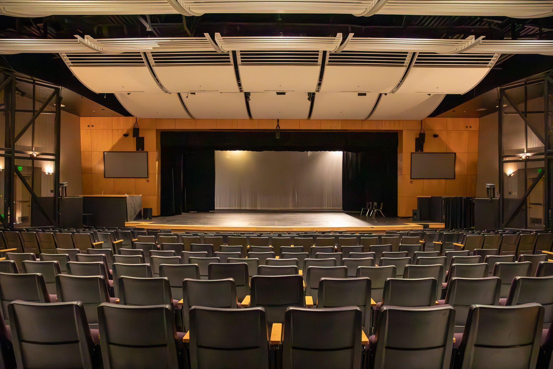Empty theater auditorium with rows of black seats facing a lit stage