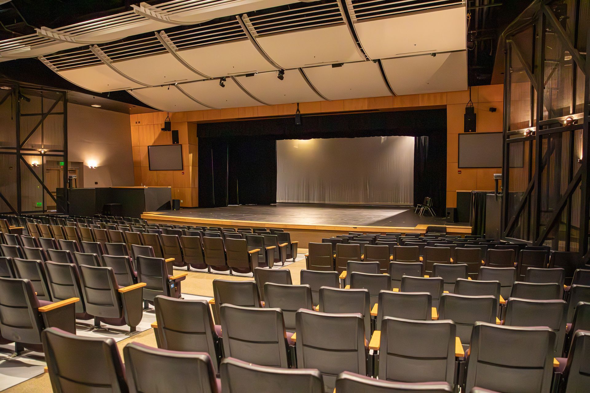Empty theater auditorium with rows of seats facing a stage and closed curtain