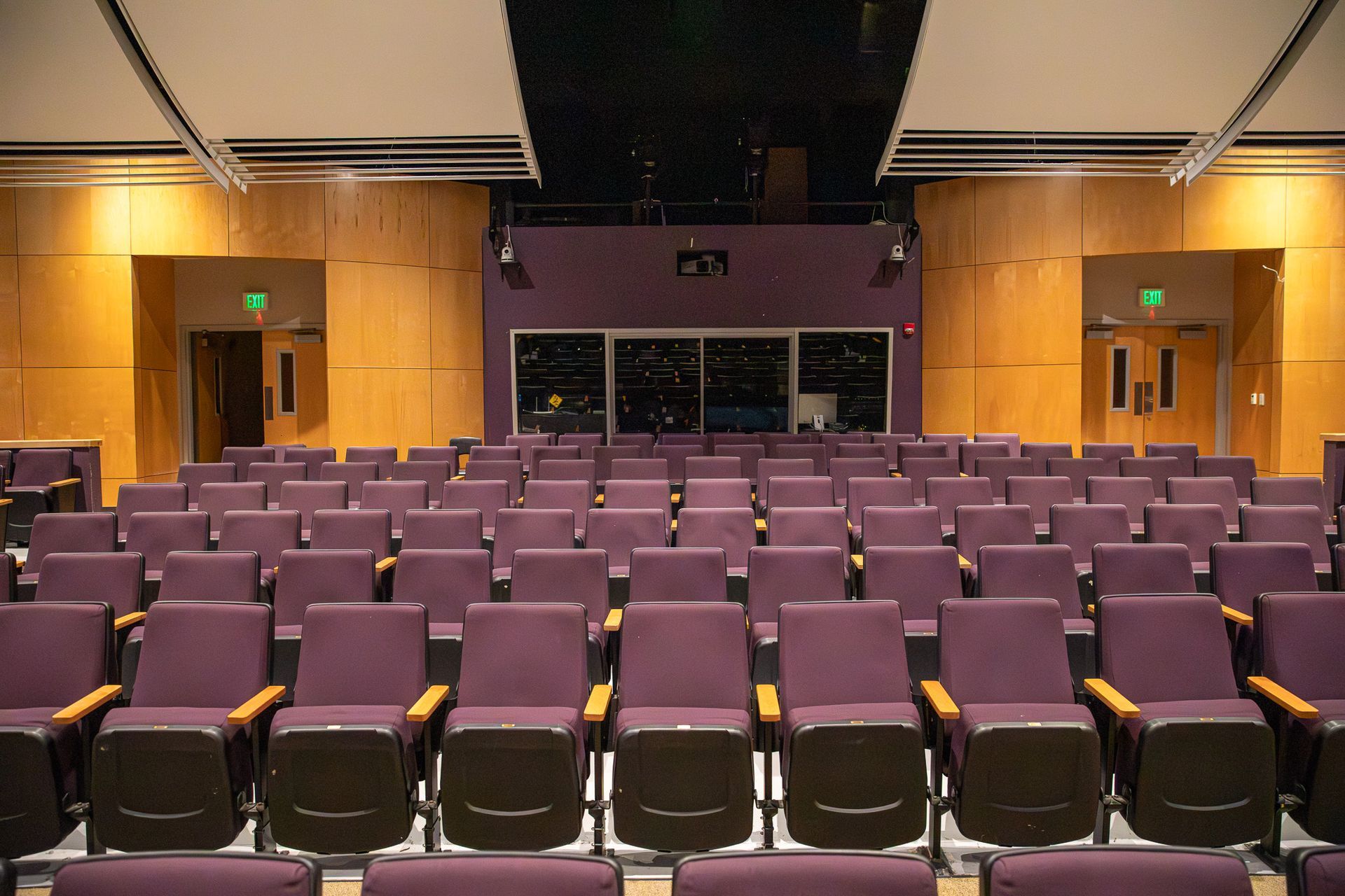 Empty auditorium with rows of purple seats facing a stage and wood-paneled walls