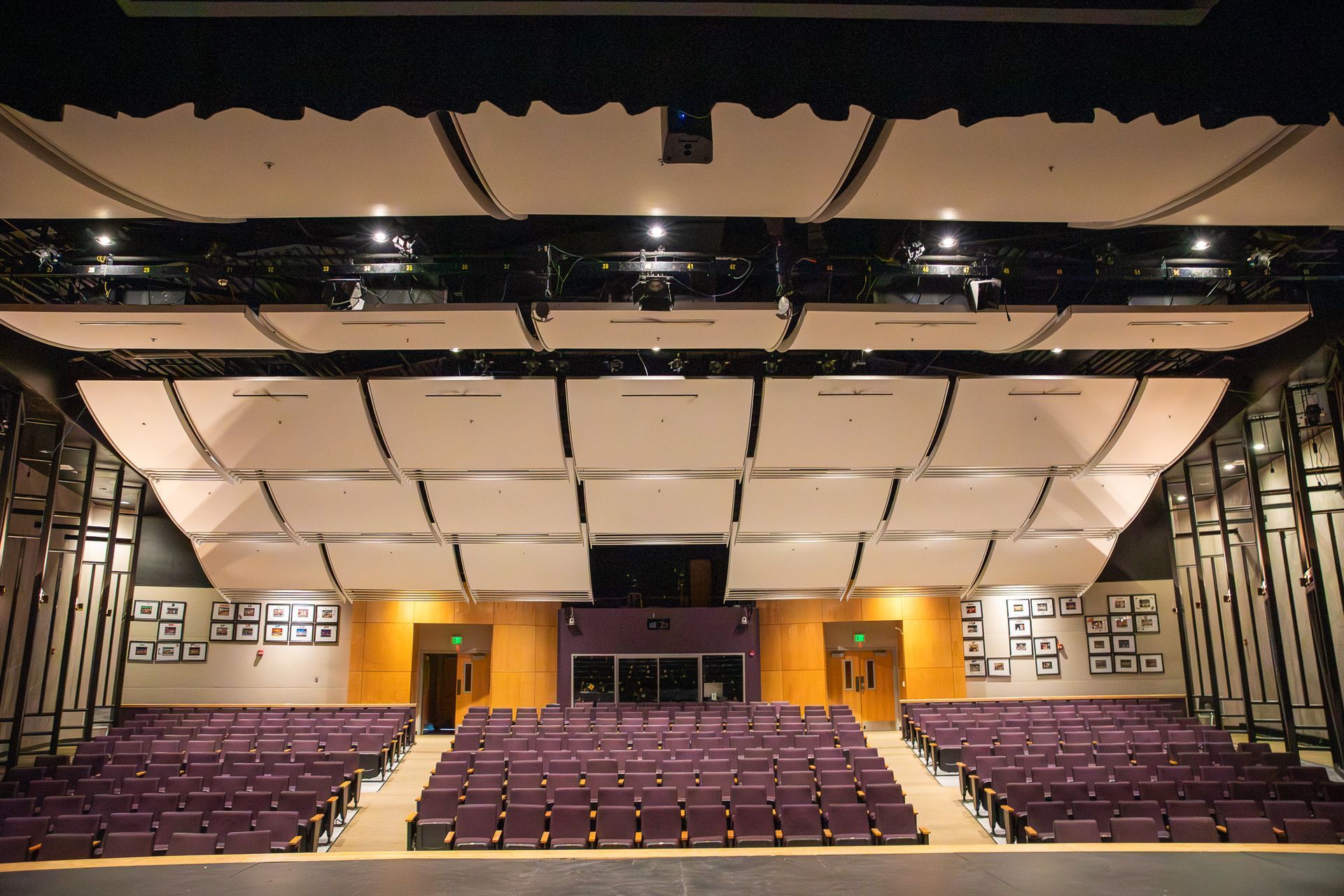 Empty theater auditorium with purple seats and a white-paneled ceiling viewed from the stage