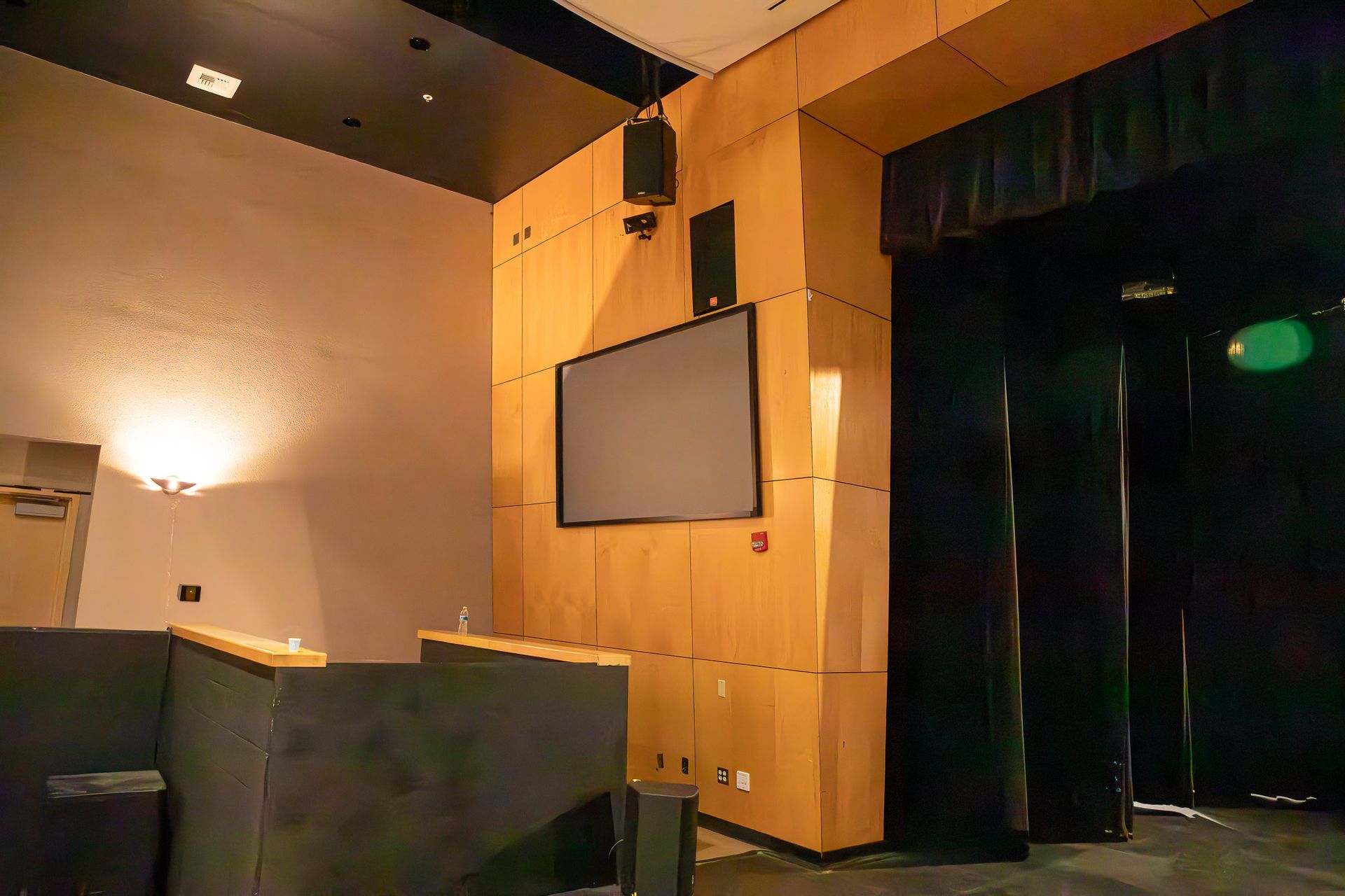 Empty auditorium stage with wood-paneled wall, projection screen, and dark curtains