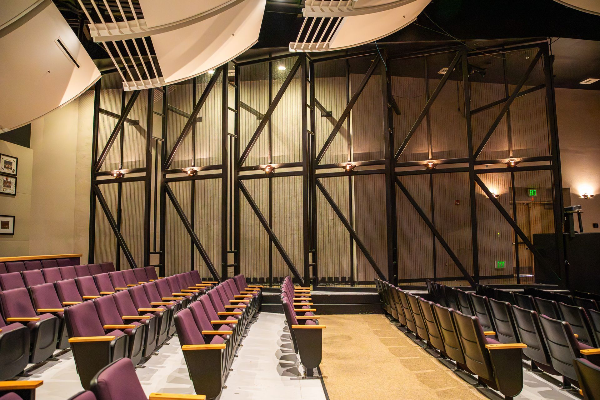 Empty auditorium with rows of purple and black seats facing a wood-paneled stage wall