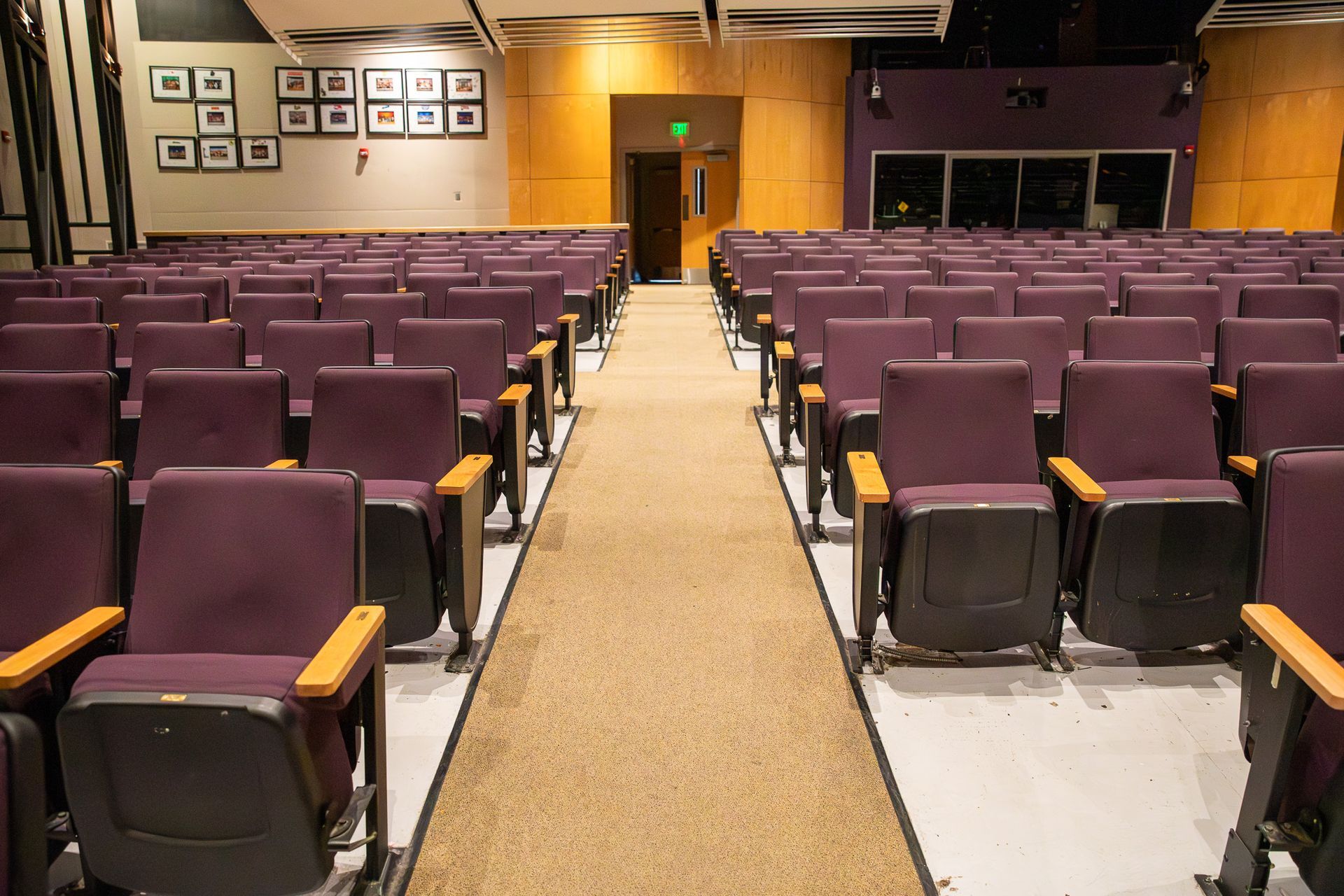 Empty auditorium with rows of purple seats and a central aisle leading to a stage area.