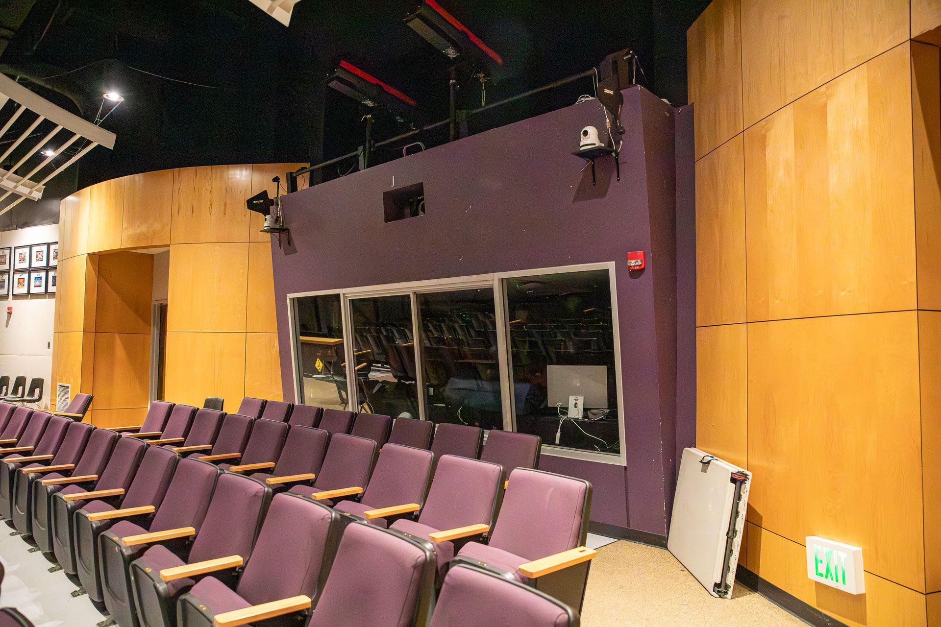 Empty theater seating facing a purple control booth and wood-paneled walls