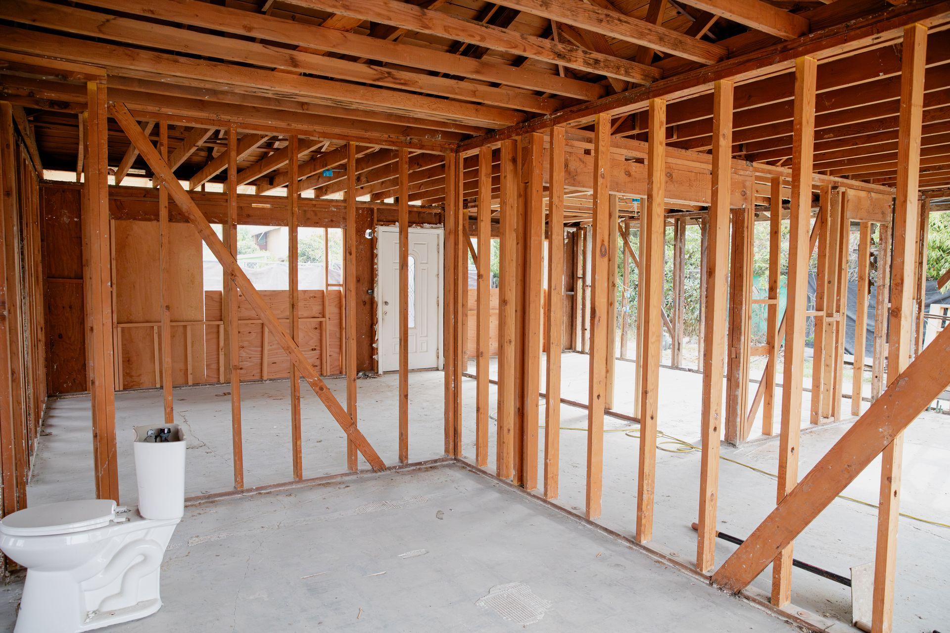 Unfinished room with exposed wooden framing, concrete floor, and a toilet near the left wall.