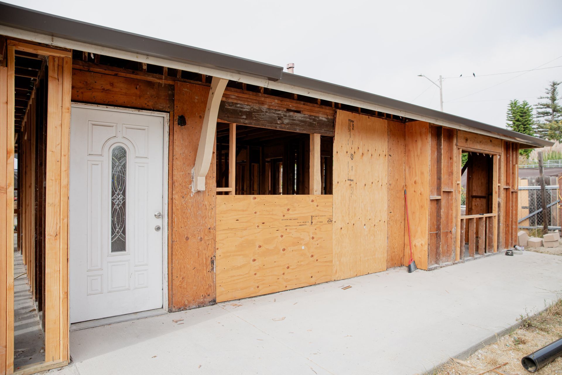Unfinished wooden house exterior with white door, windows, and concrete walkway