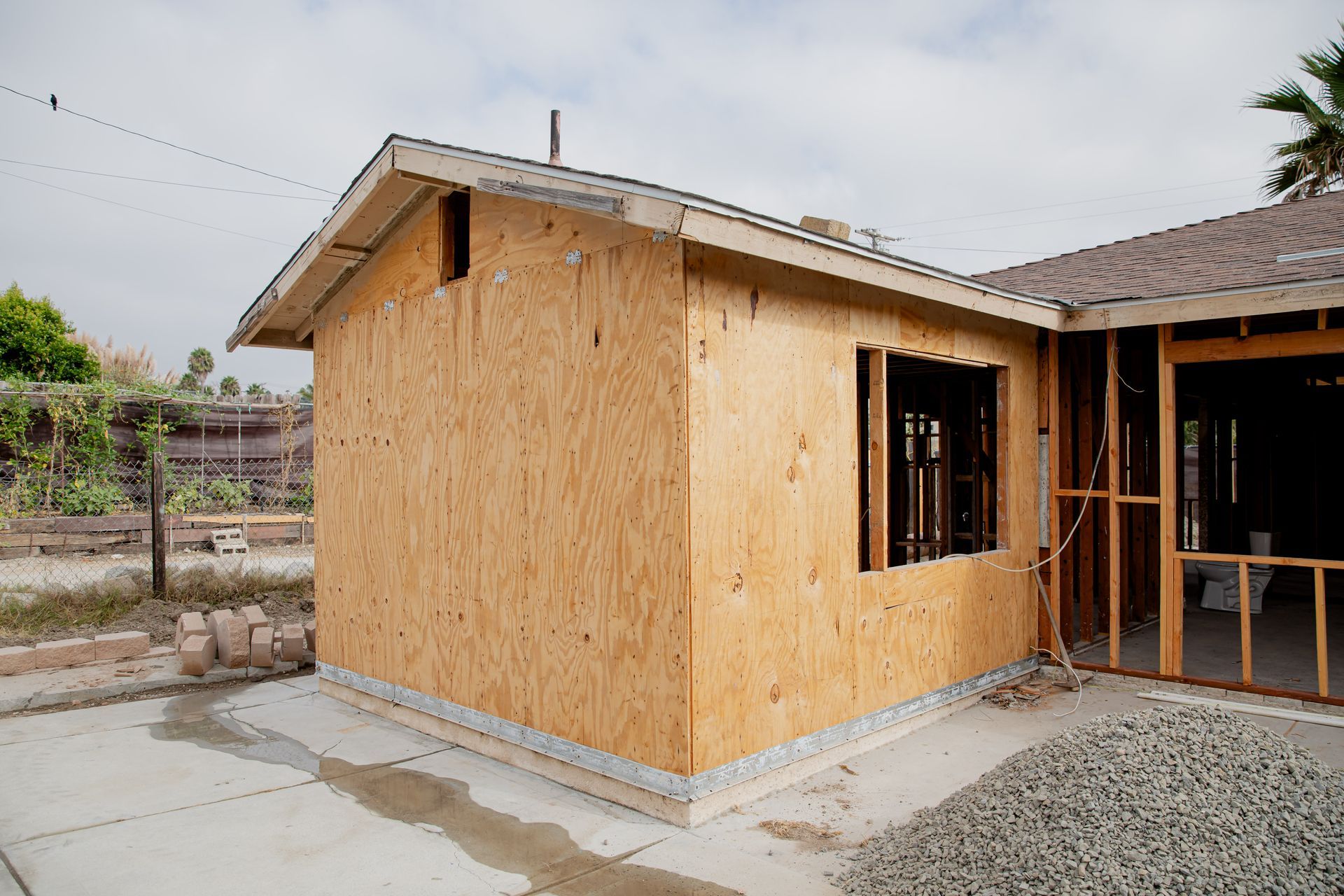 Partially built house with plywood siding, a window opening, and concrete slab in a residential lot