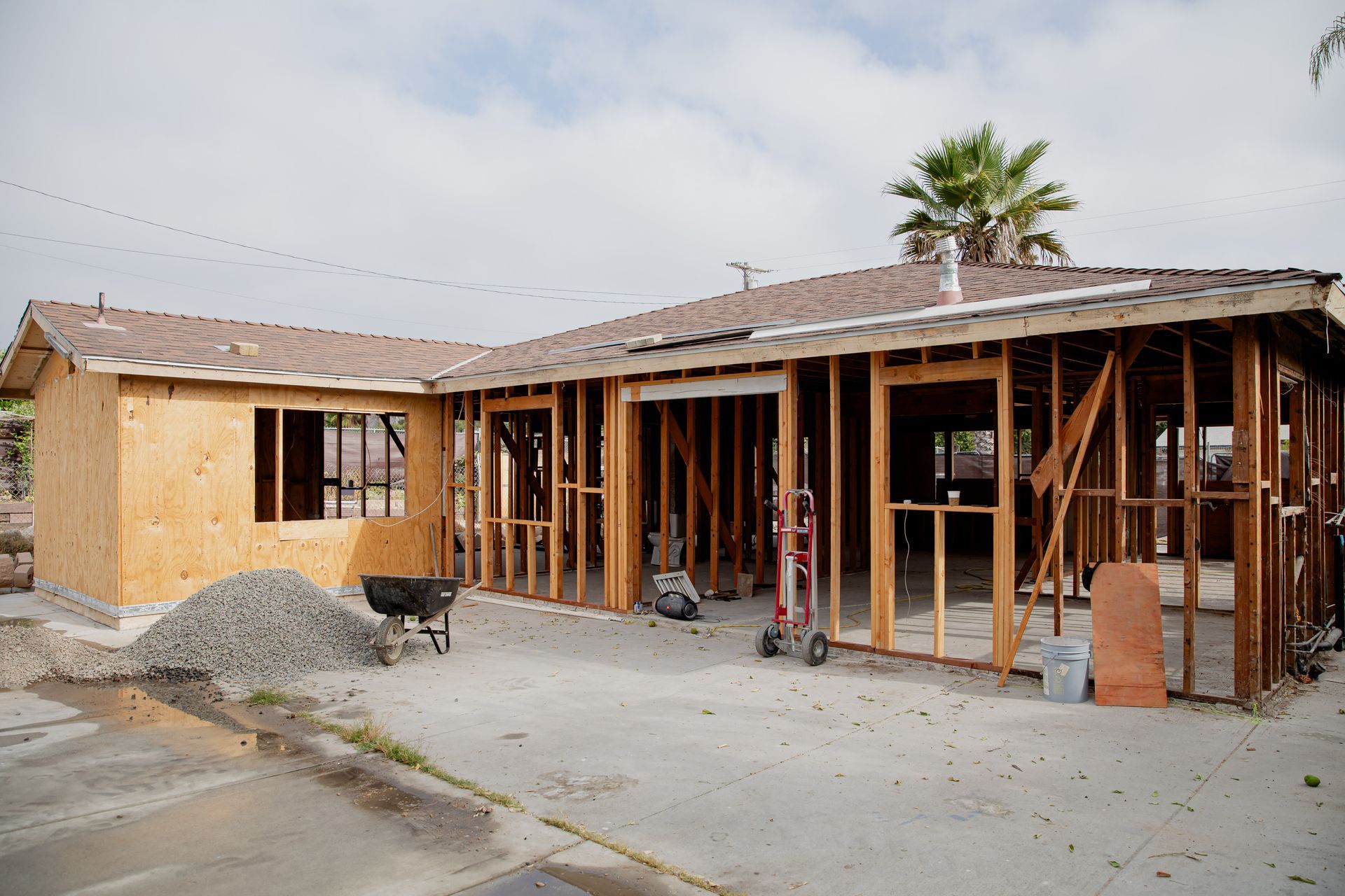 Partially framed house under construction with exposed wood, tan siding, and piles of dirt in the driveway