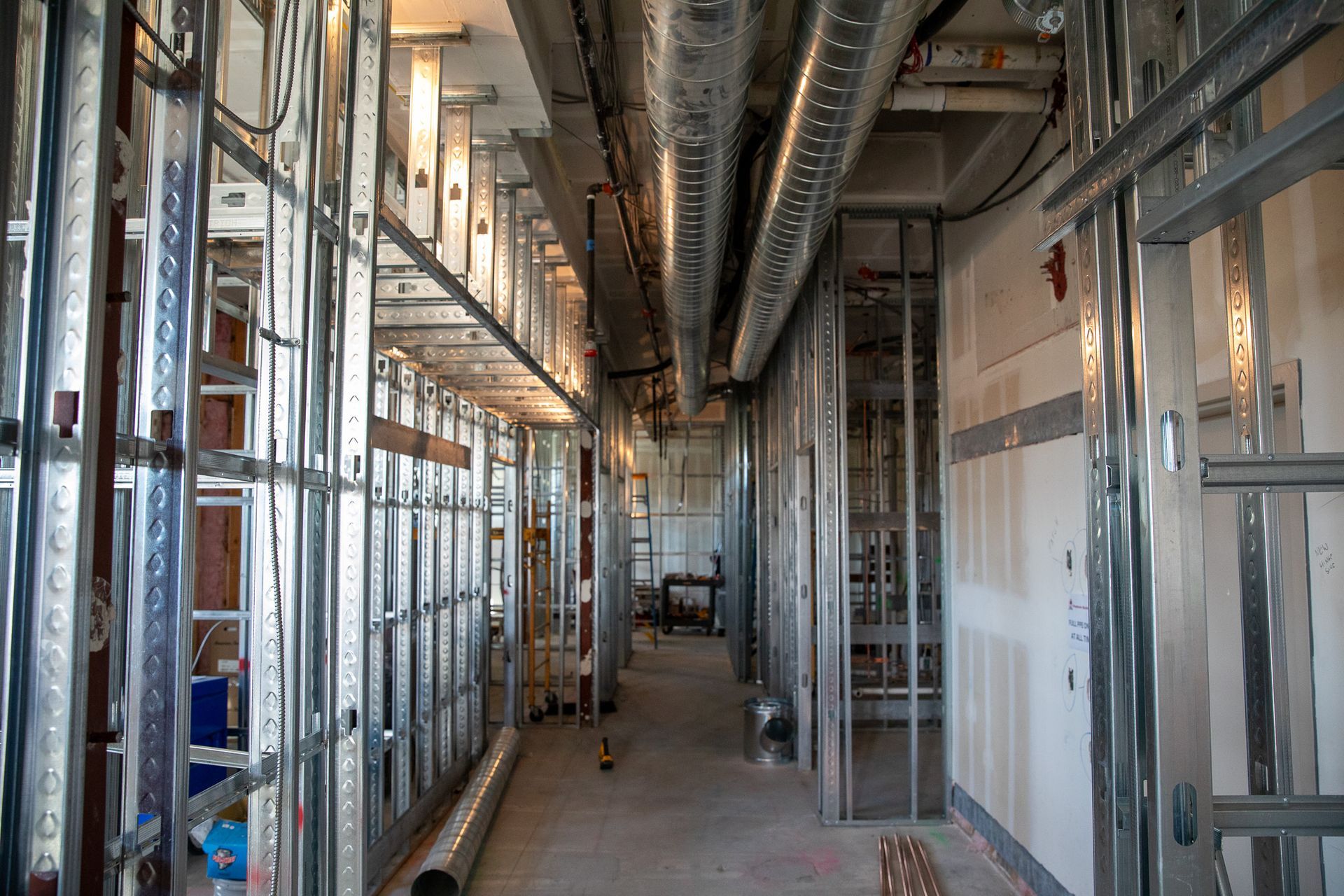 Unfinished building hallway with exposed metal framing, ducts, and construction materials.