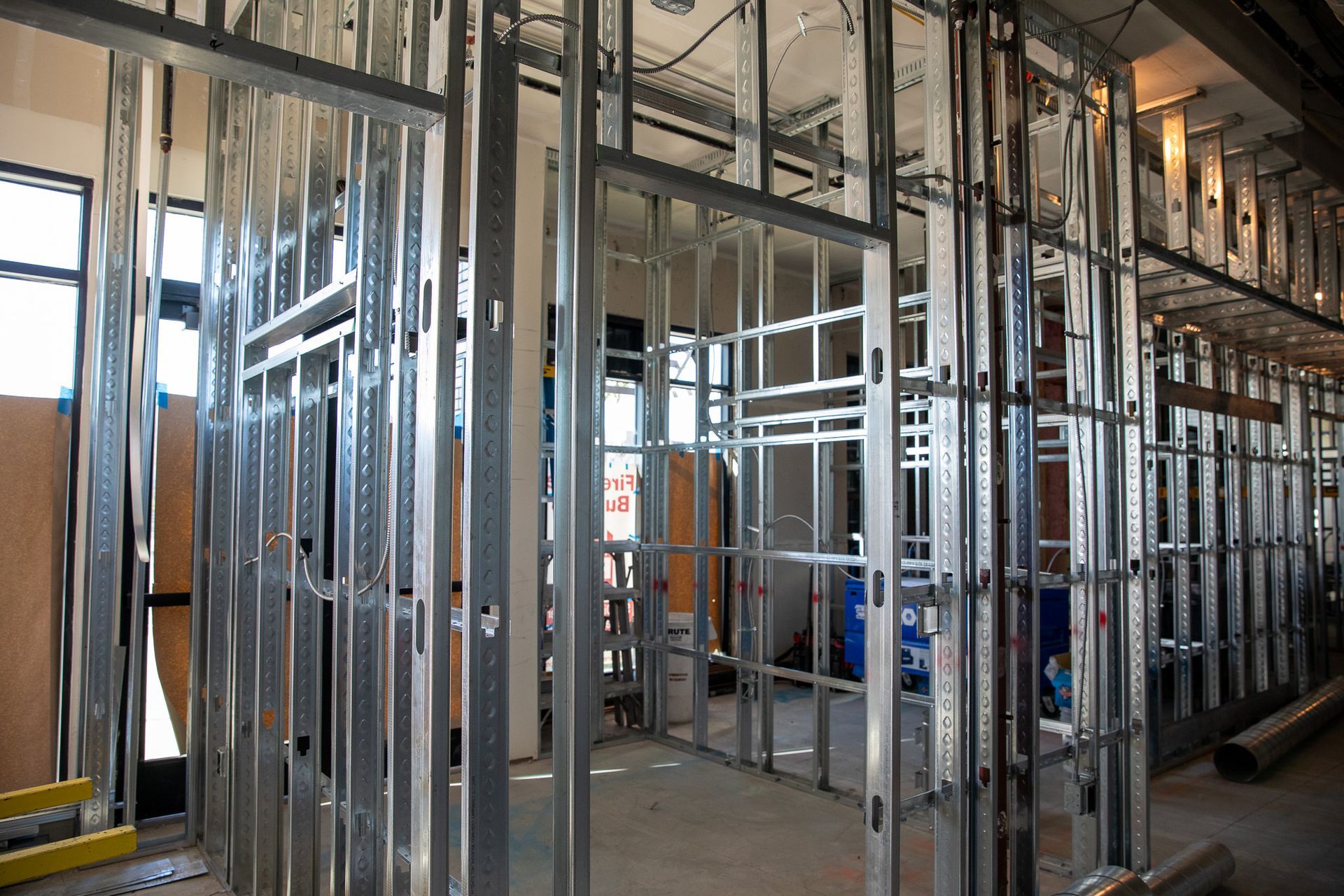 Exposed metal wall framing inside a building under construction, with unfinished floors and windows.