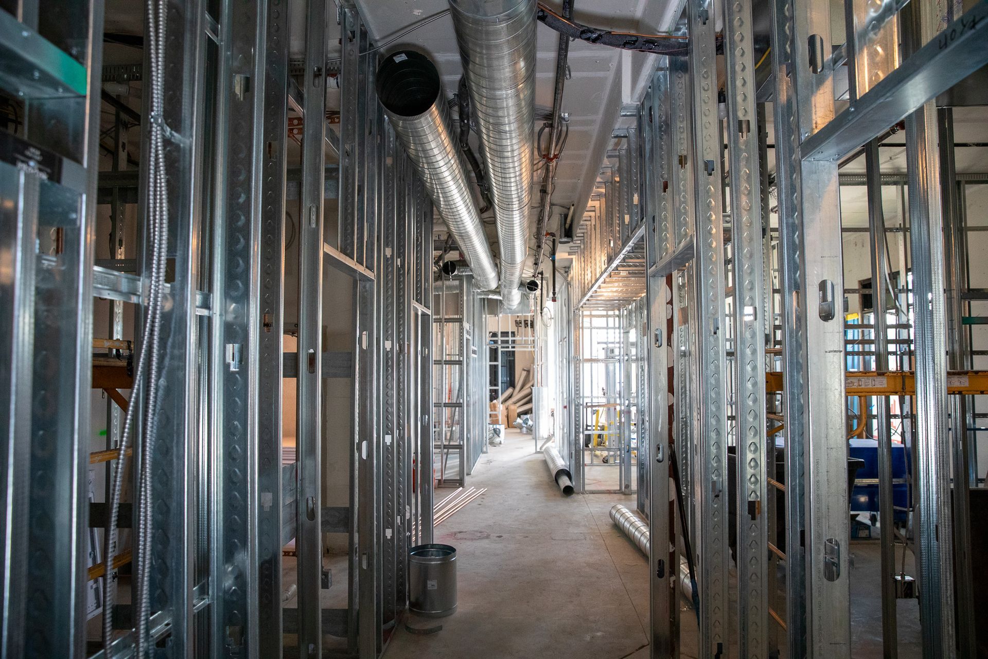 Interior of a building under construction with exposed metal framing, ducts, and pipes in a narrow corridor
