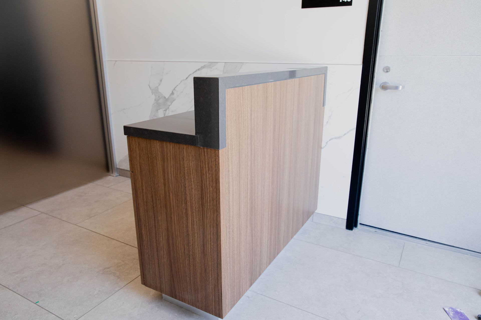 Small modern reception desk with wood and white panels in a lobby near a door