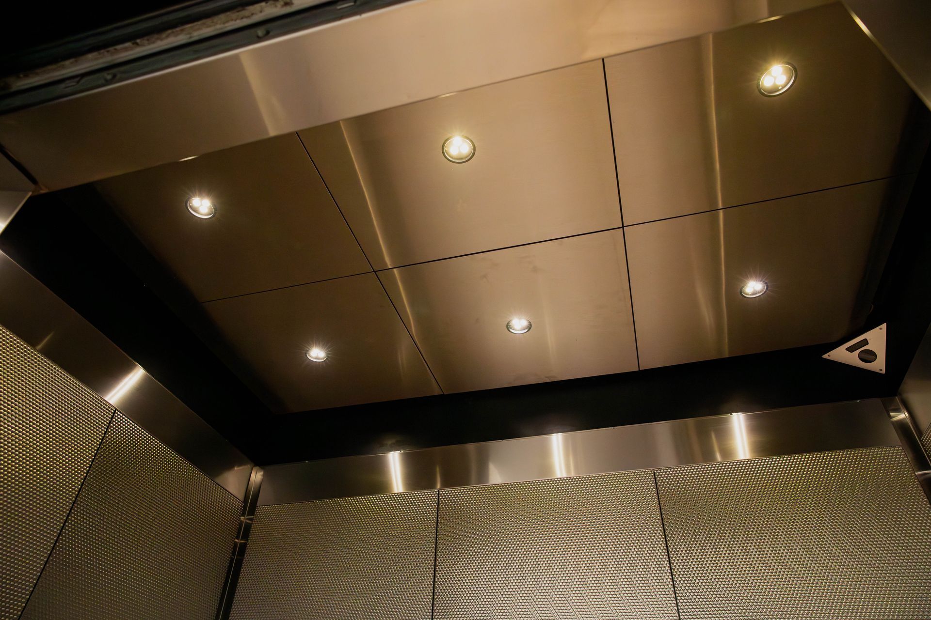 Ceiling of an elevator with recessed lights and brushed metal panels